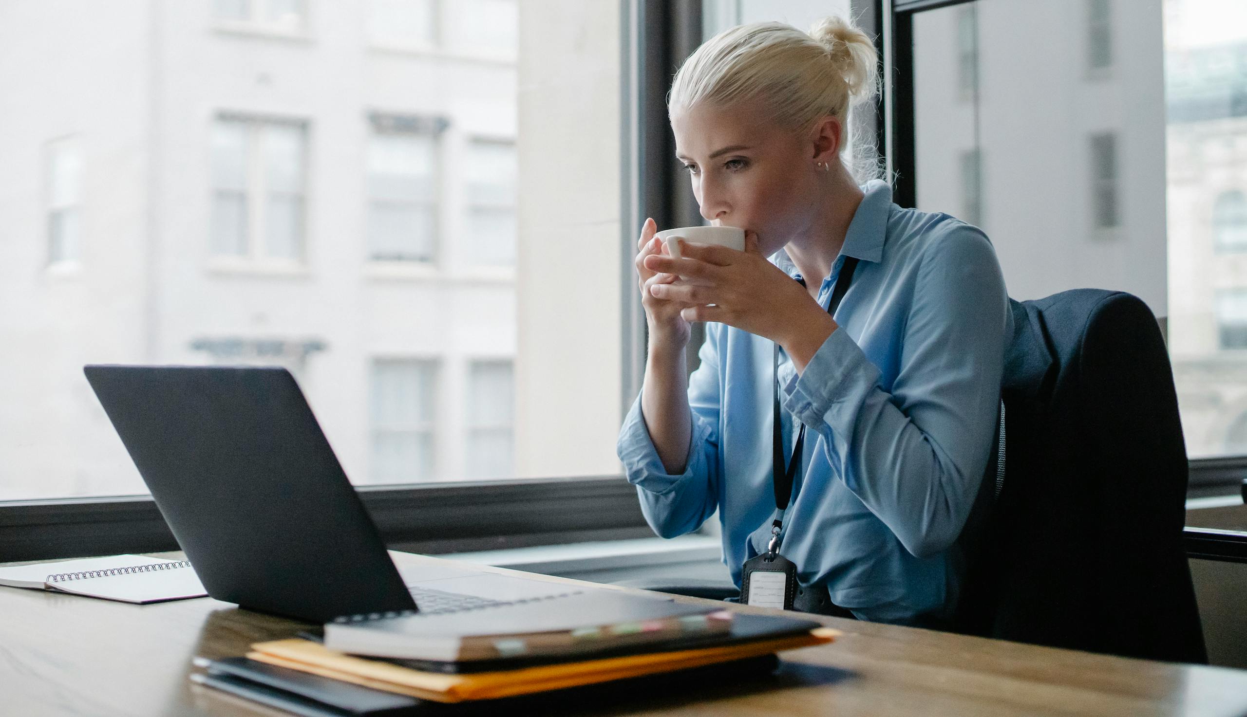 Young serious female worker in formal clothes having mug of hot drink while working in company
