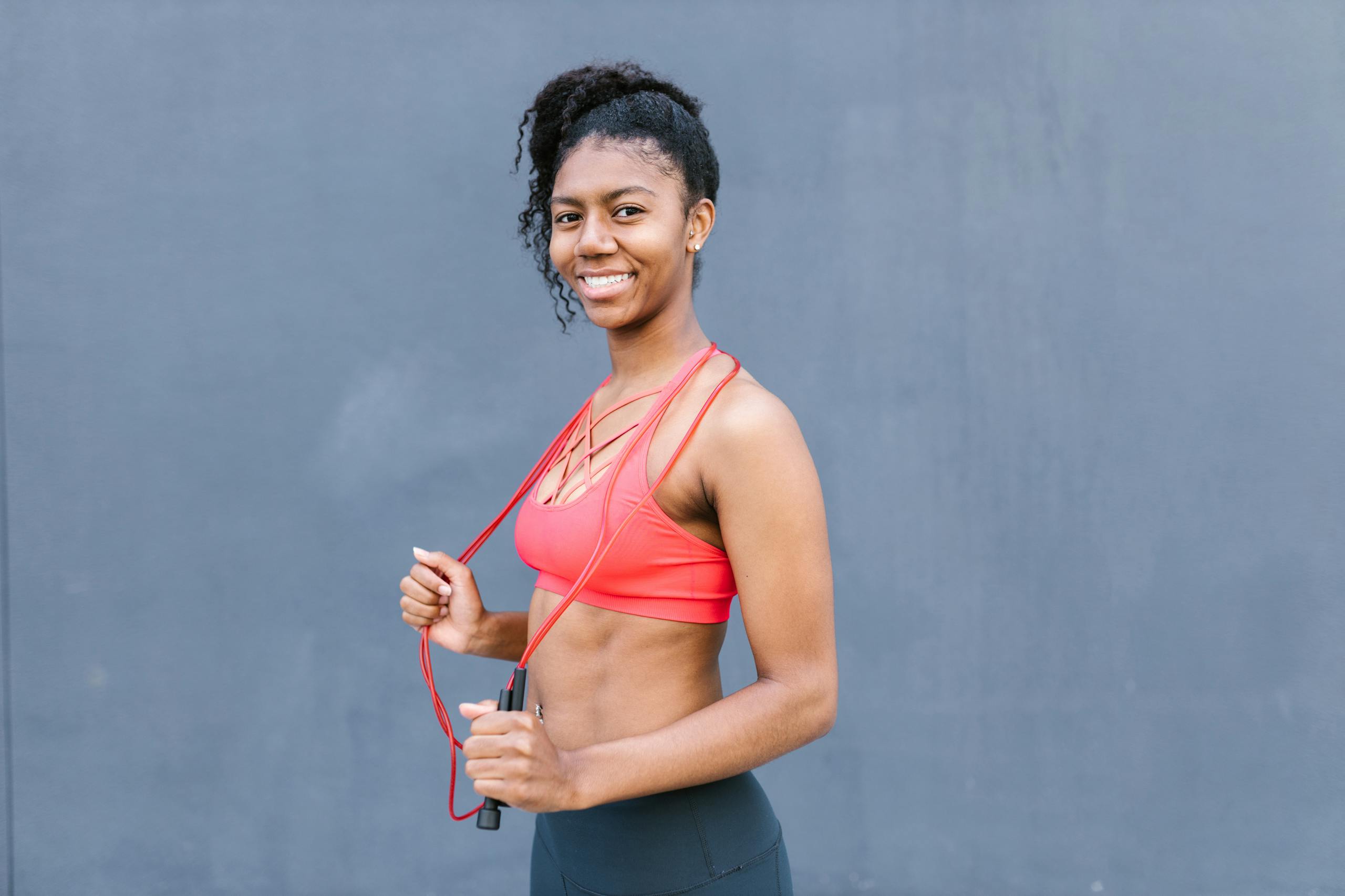 Young woman with curly hair in sportswear holding a jump rope and smiling confidently.