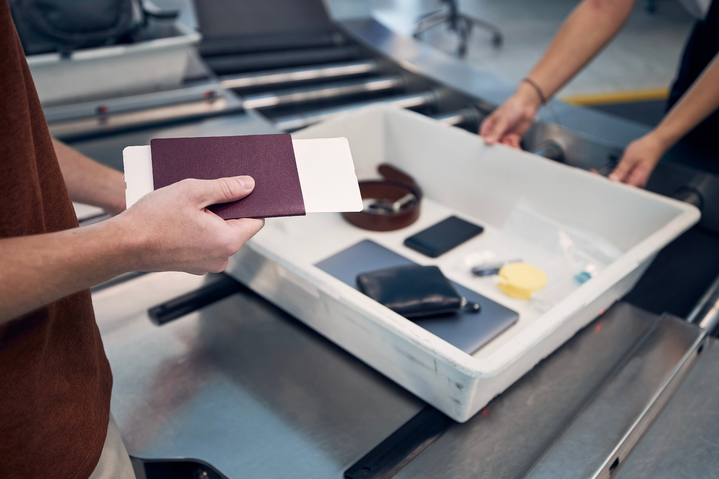 Passenger holding passport against personal Items, liquids, and laptop in container at airport security check.