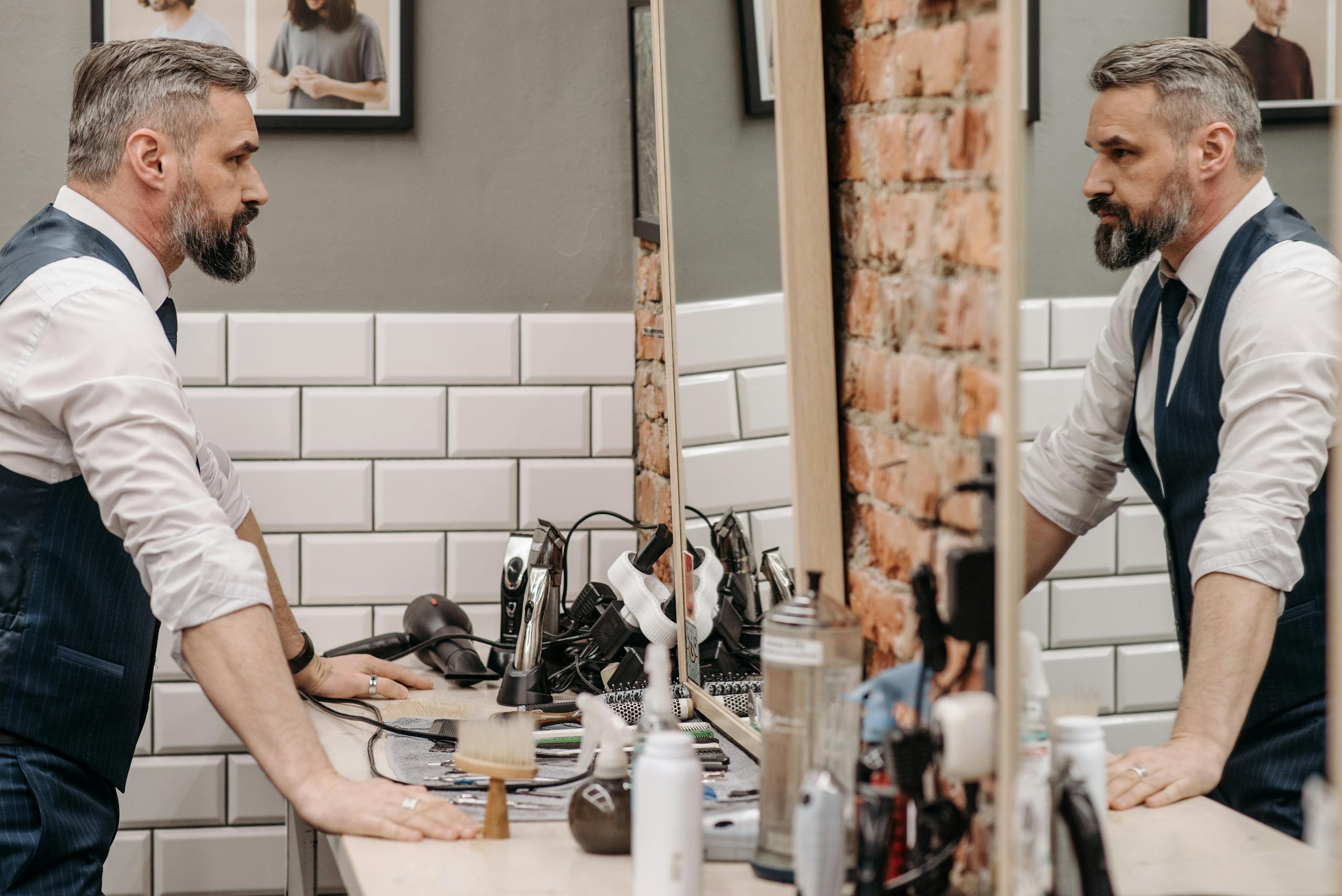 A bearded gentleman examines his reflection in a stylish barbershop setting.