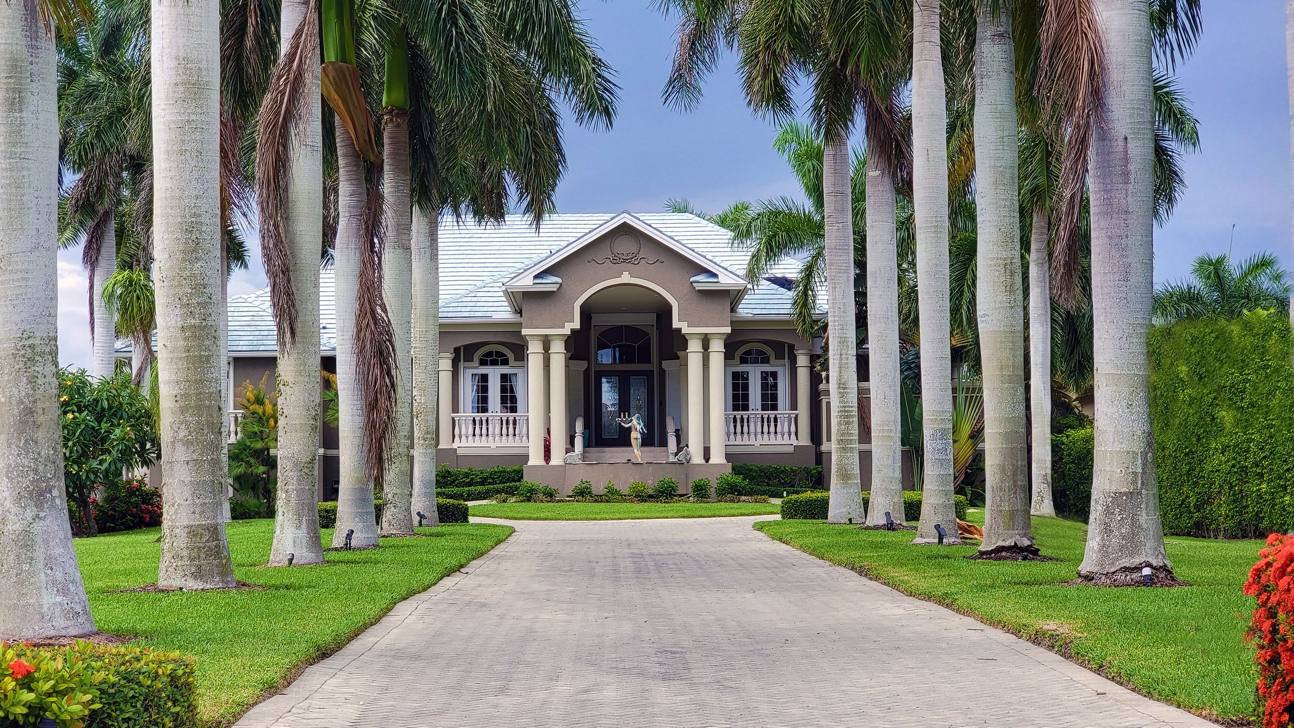 A beautiful residential house with palm trees lining the driveway under a clear sky.