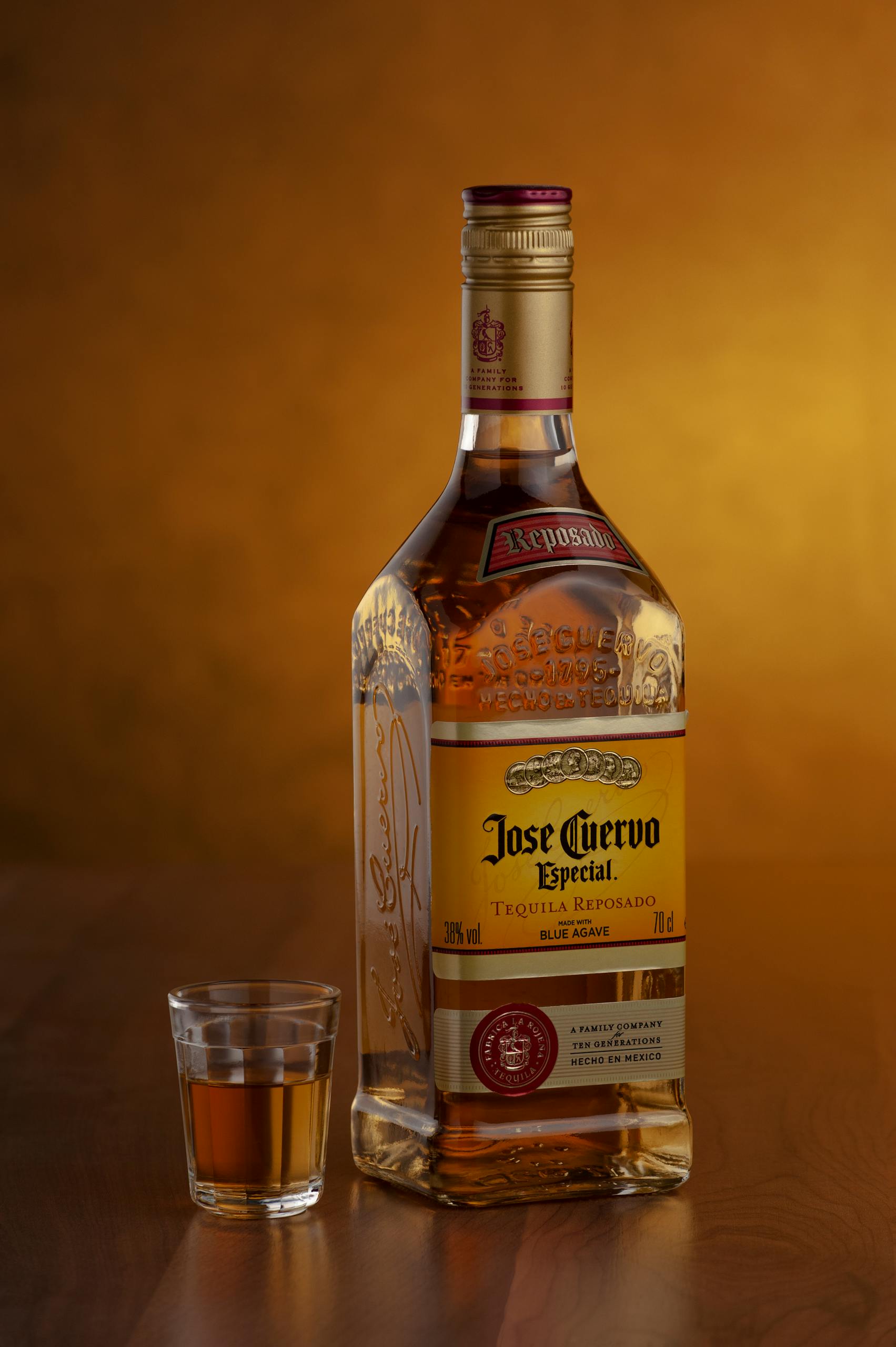 A bottle of Jose Cuervo tequila beside a filled shot glass against a warm background.