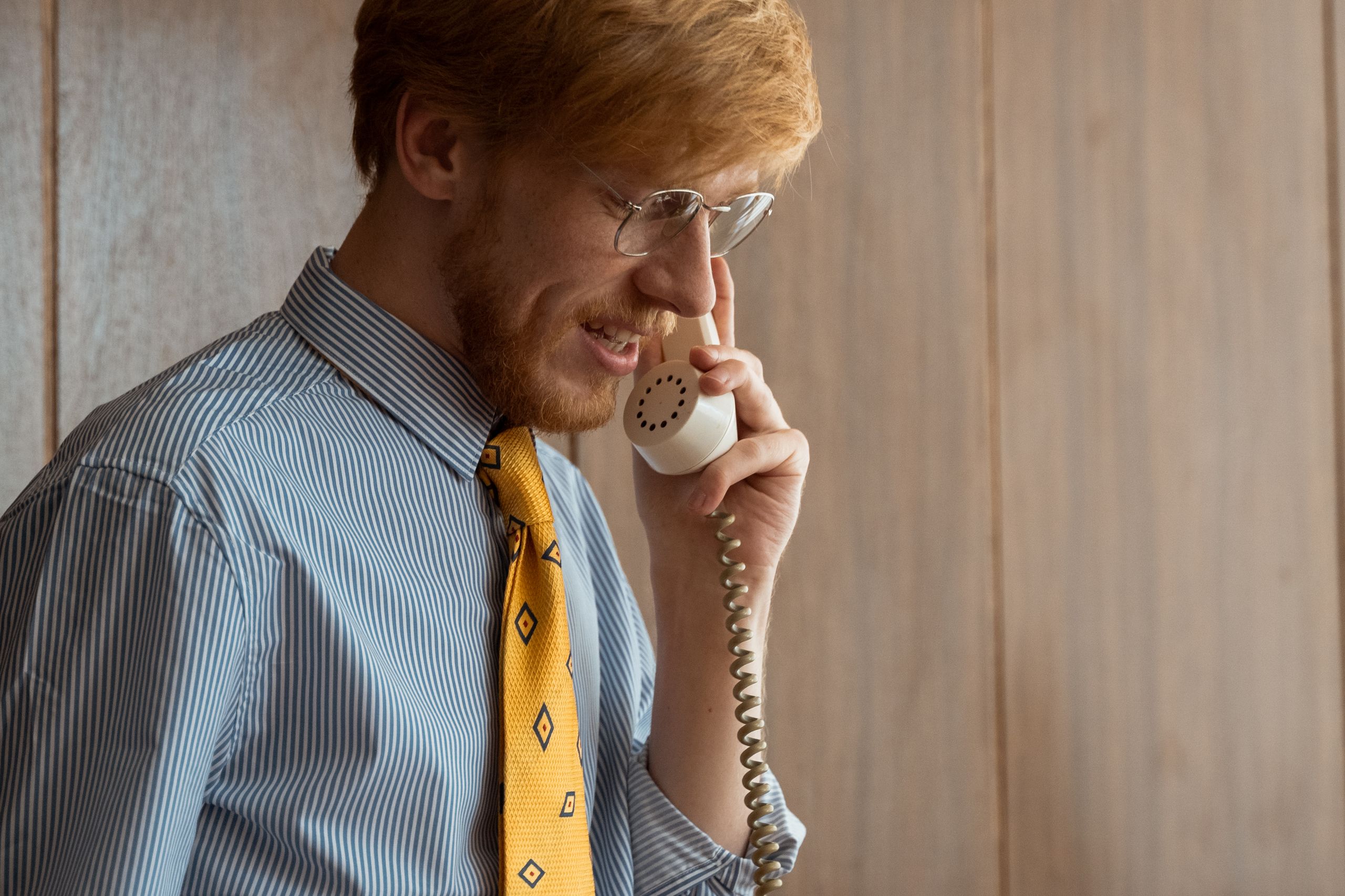 A businessman with glasses making a phone call in a retro office setting.
