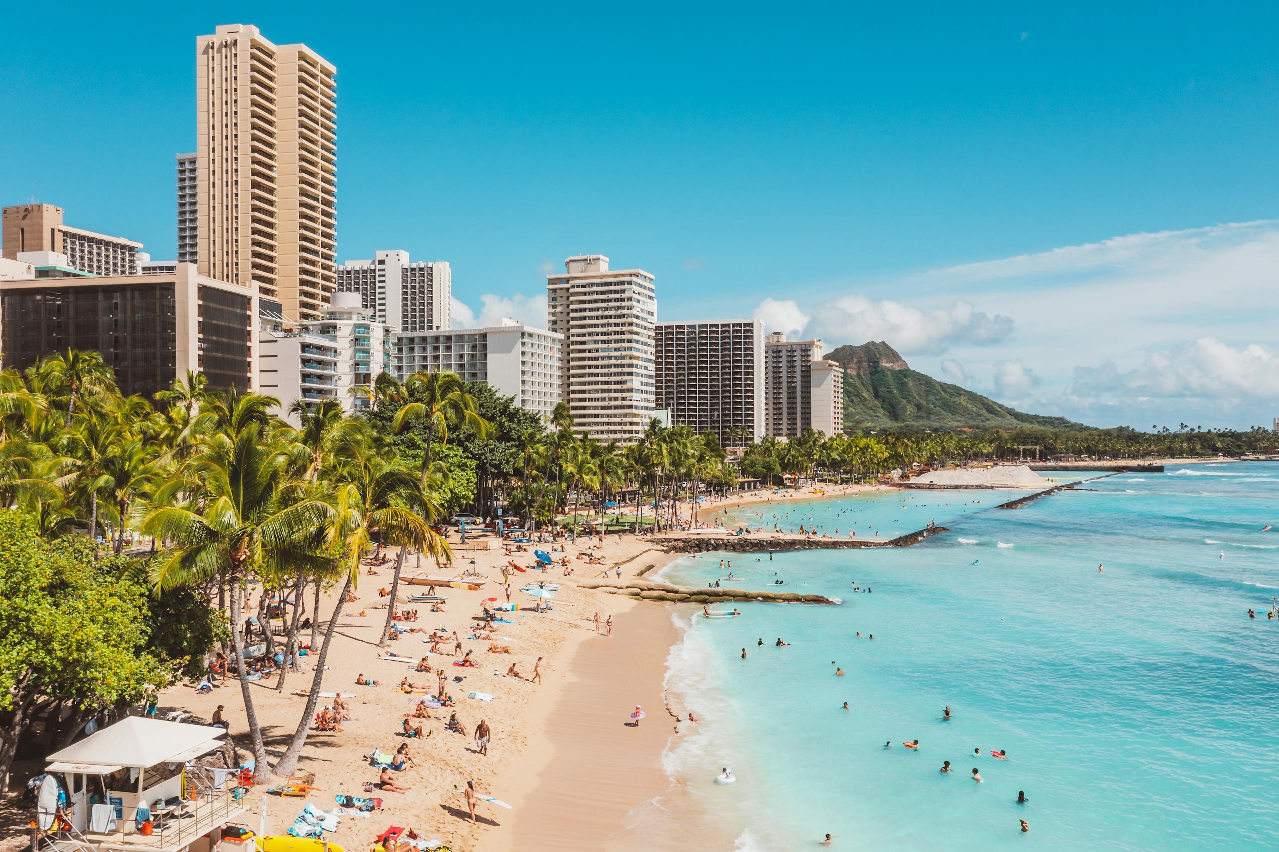 A bustling Waikiki Beach scene with skyscrapers and Diamond Head in the background, highlighting a popular travel destination.