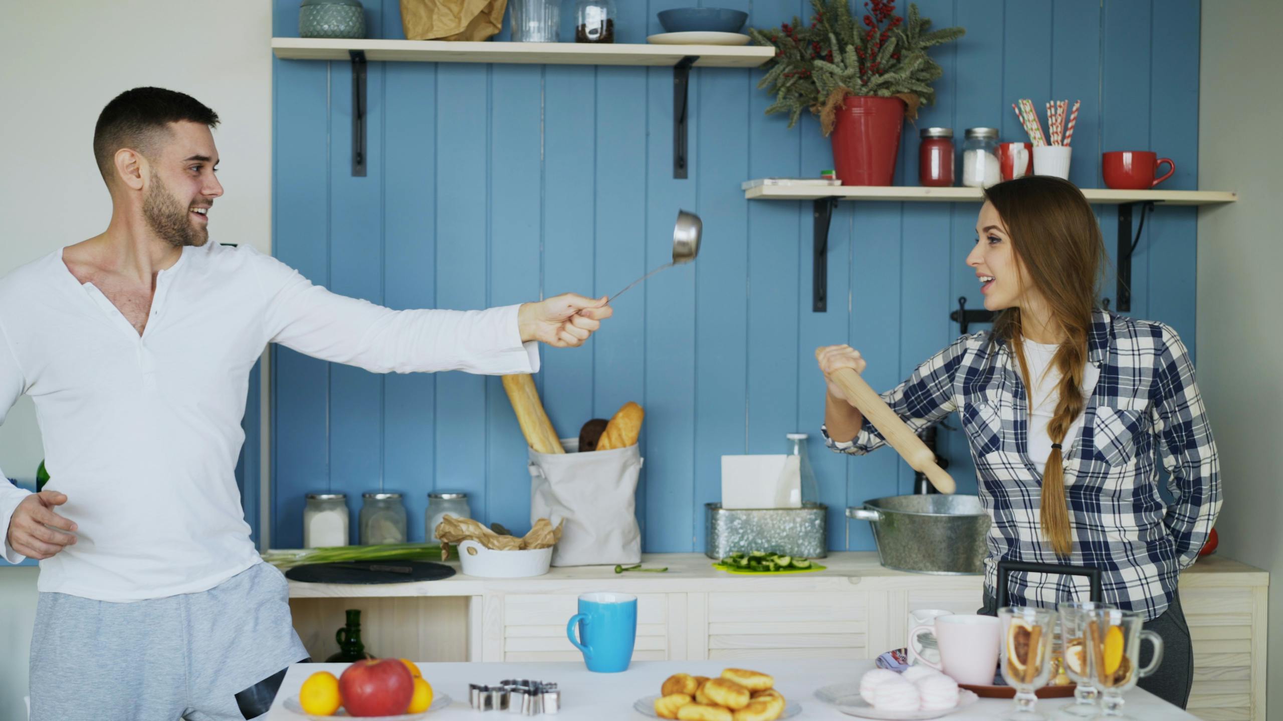 A cheerful couple playfully cooking together in a modern kitchen, engaging in a fun cooking duel.