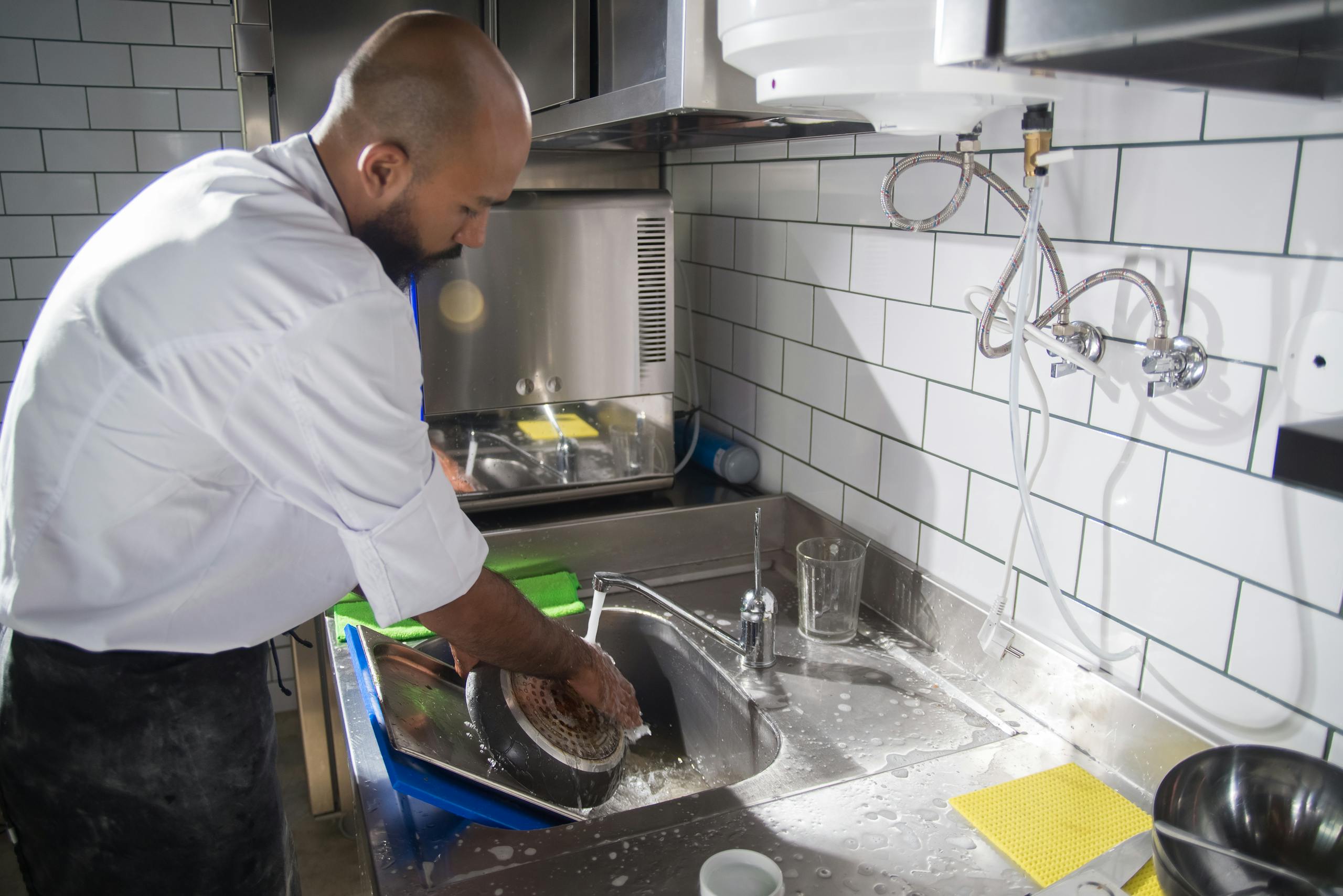 A chef cleans kitchen utensils in a stainless steel sink, maintaining hygiene standards.