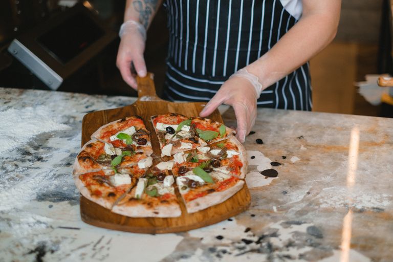 A chef holds a serving board with a freshly made gourmet pizza, garnished with basil and cheese.