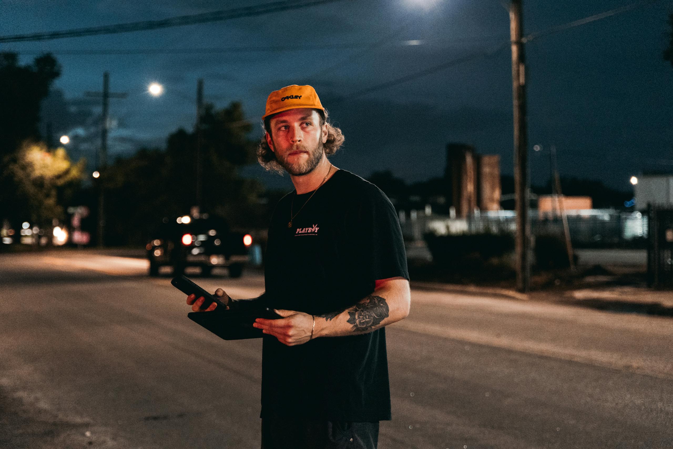 A cinematographer holds camera gear on an urban street at night, ready for filming.