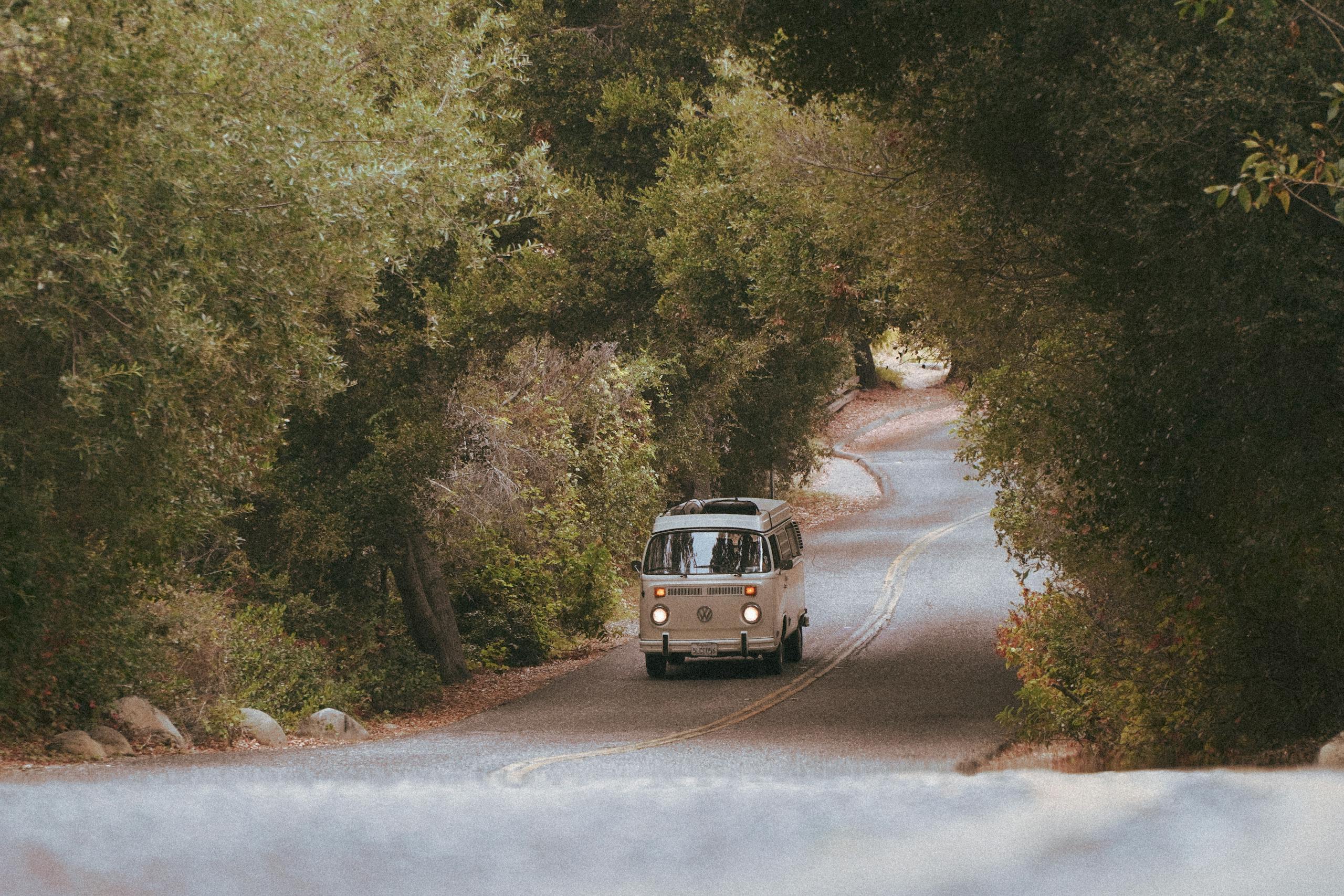 A classic white van traveling along a winding, tree-lined forest road, creating a serene and nostalgic vibe.