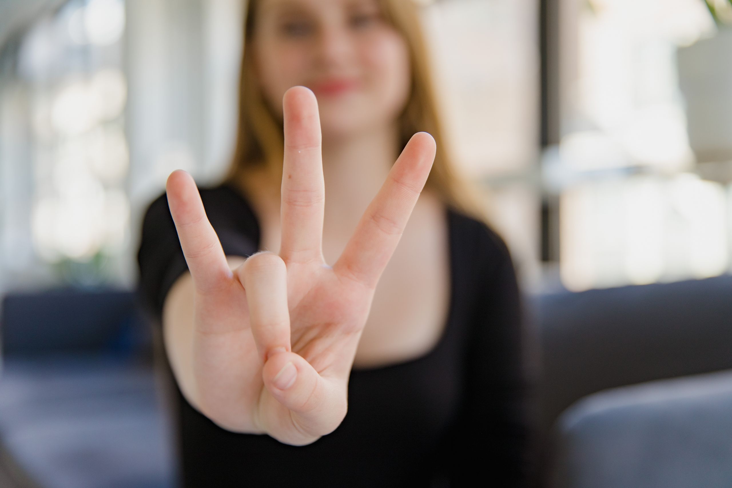 A close-up image of a woman making the ASL sign for 'I Love You' with focus on the hand gesture.
