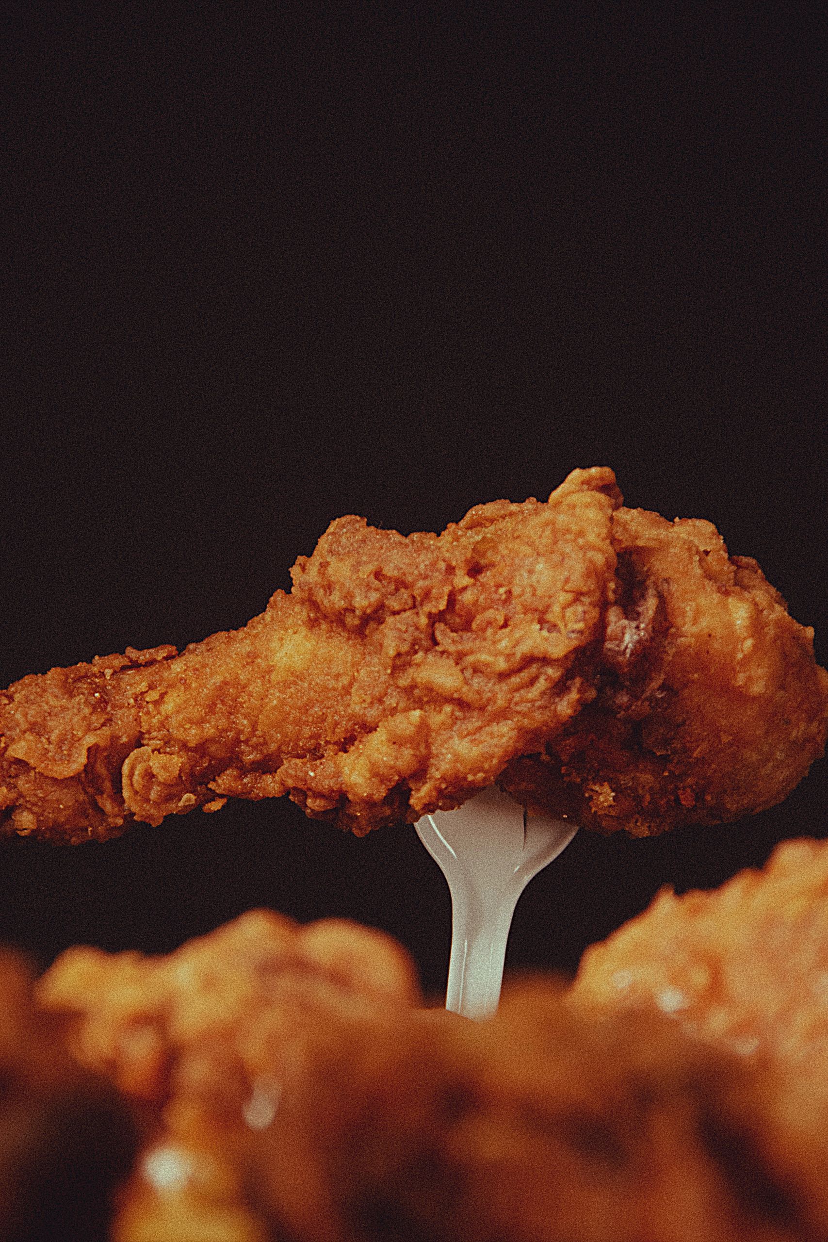 A close-up of a crispy fried chicken wing on a fork, highlighting its texture.