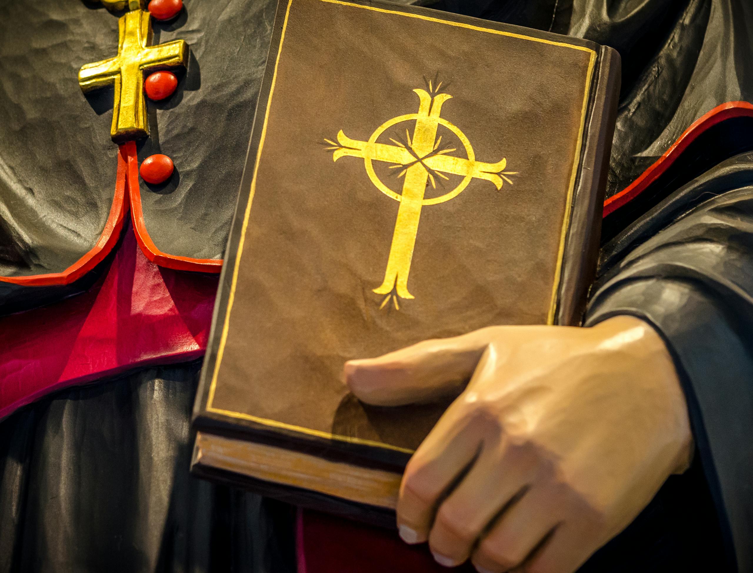 A close-up of a religious book with a cross held by a statue, symbolizing faith and spirituality.