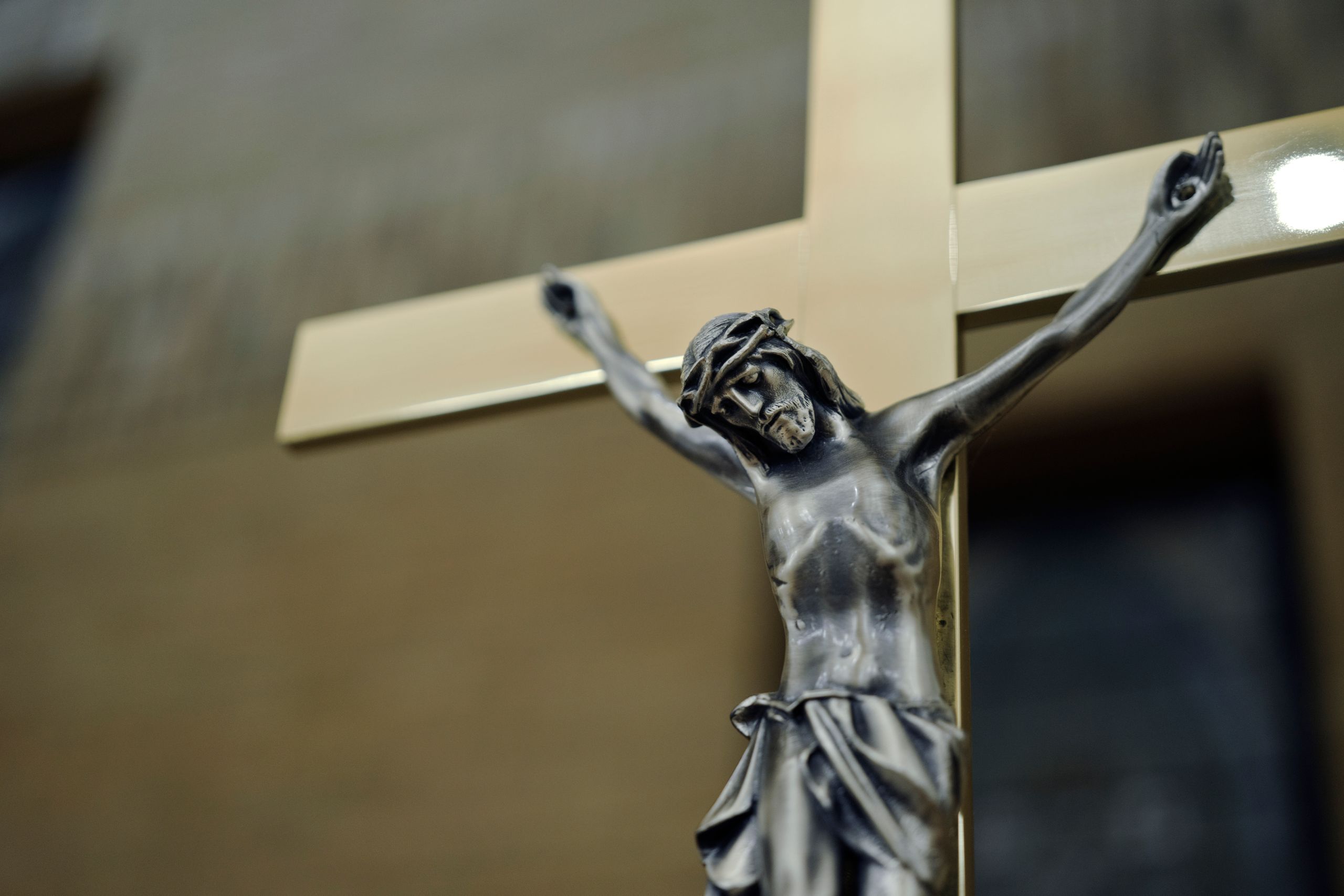 A close-up of a sacred silver crucifix on a golden cross indoors, depicting Christian symbolism.