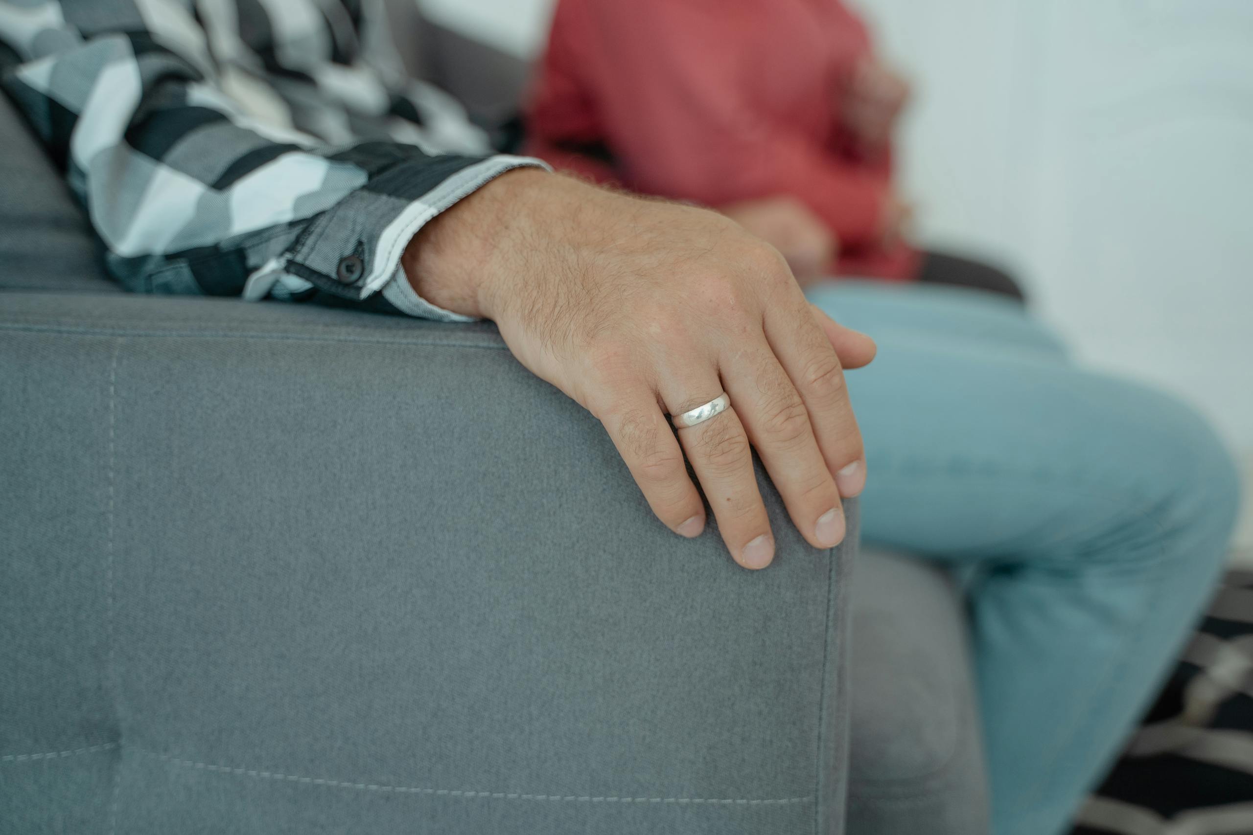 A close-up view of adult hands resting on a couch wearing a wedding ring indoors.