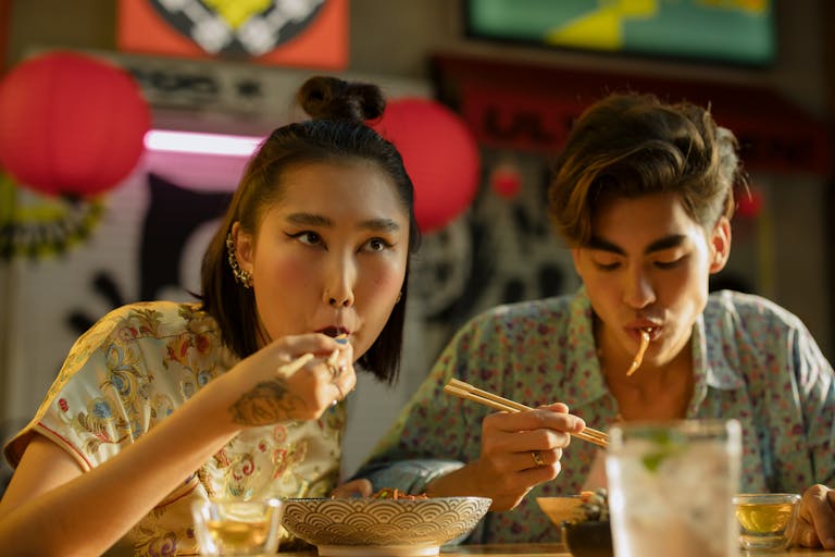 A couple enjoys a meal with chopsticks in an Asian restaurant with vibrant decor.