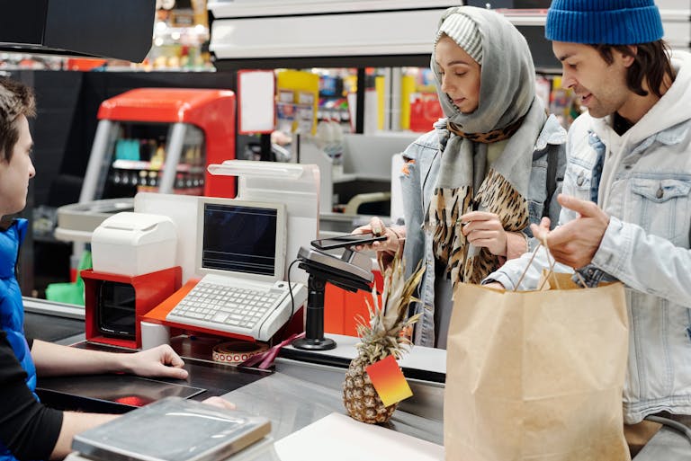 A couple in a supermarket checkout using mobile payment with a cashier. Modern retail technology.