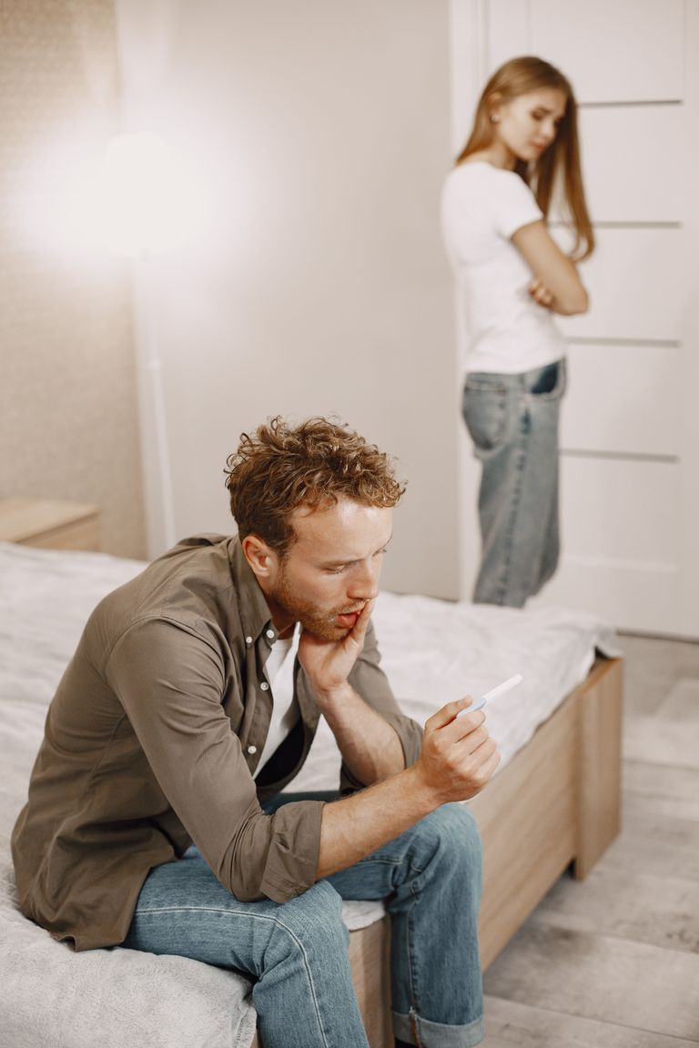 A couple in discussion after reviewing a pregnancy test result, showing mixed emotions.
