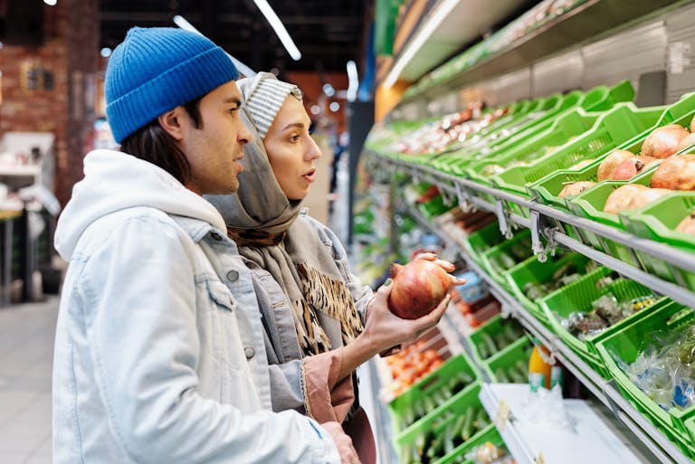 A couple selecting pomegranates in a grocery store aisle filled with fresh produce.