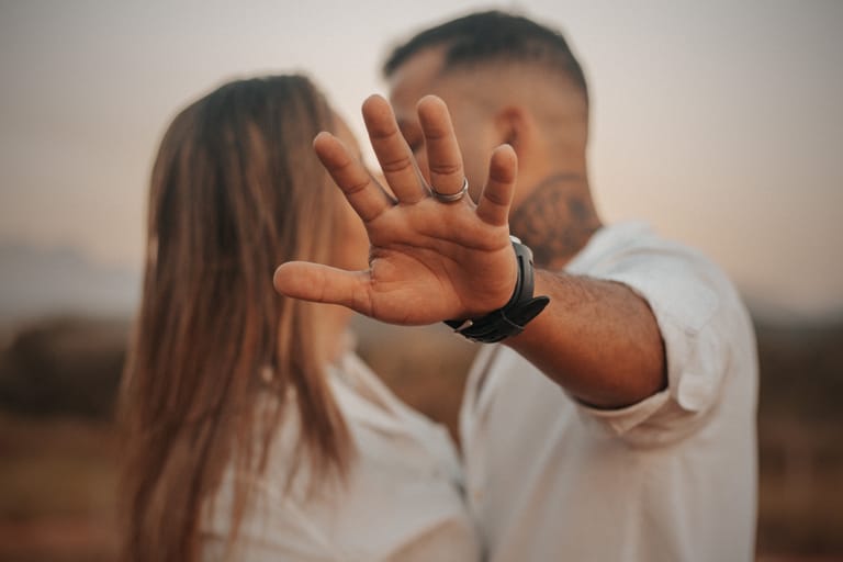 A couple shares an intimate moment outdoors, with a hand gesture adding mystery and emotion.