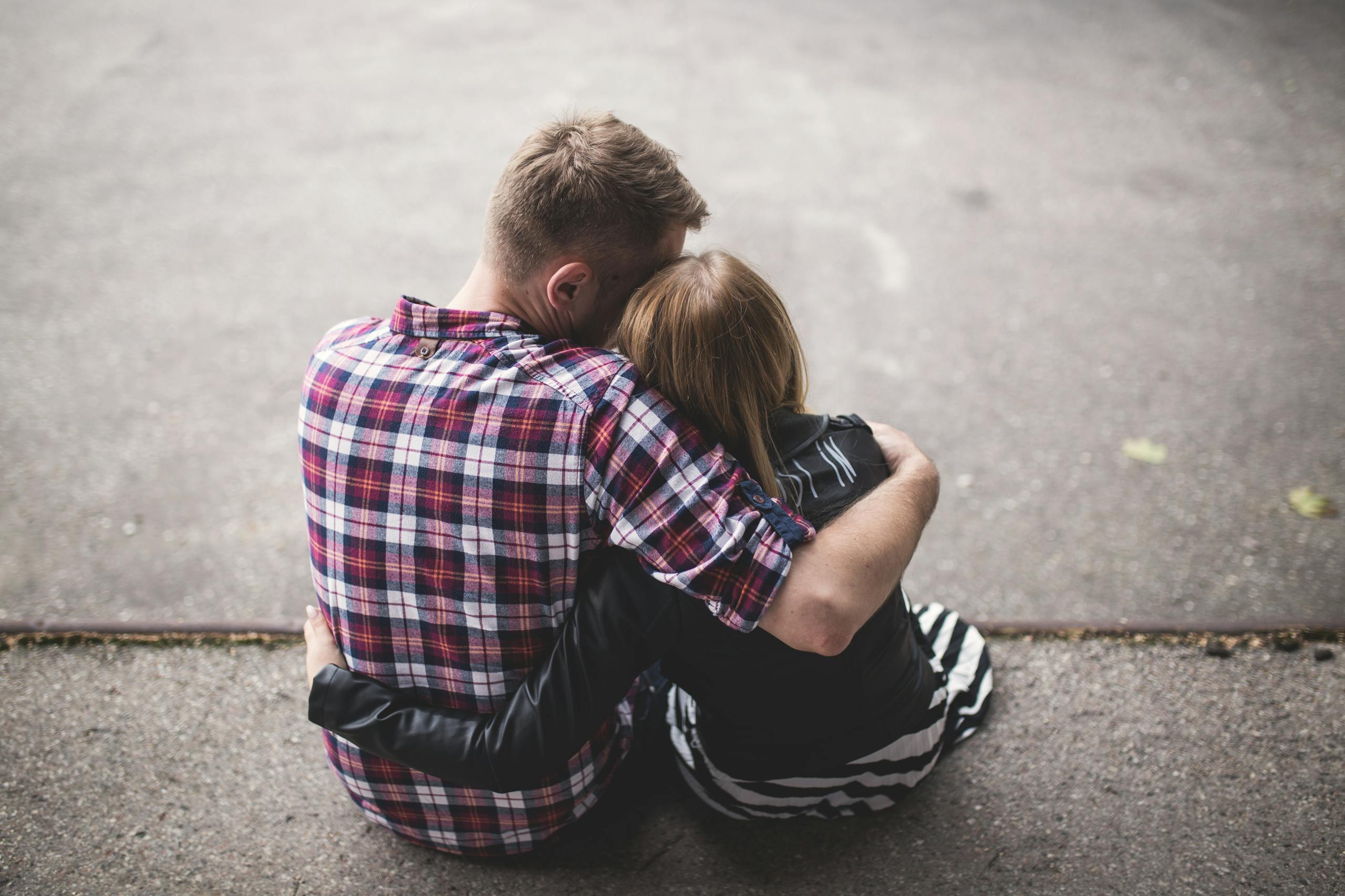A couple sitting closely together on the ground, sharing an intimate embrace.