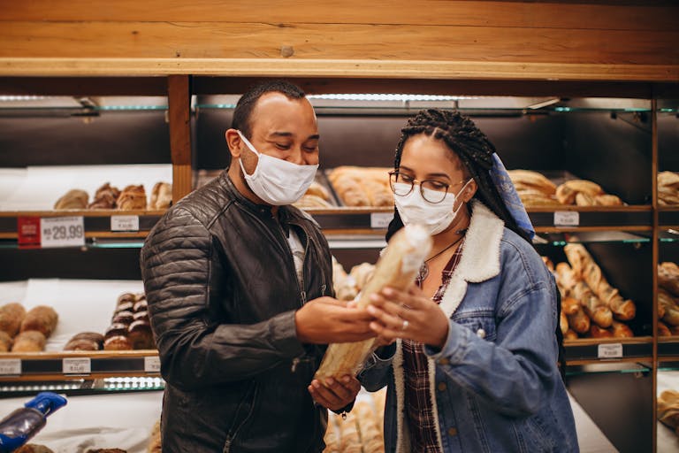 A couple wearing masks selecting bread in a bakery. Indoors during pandemic.