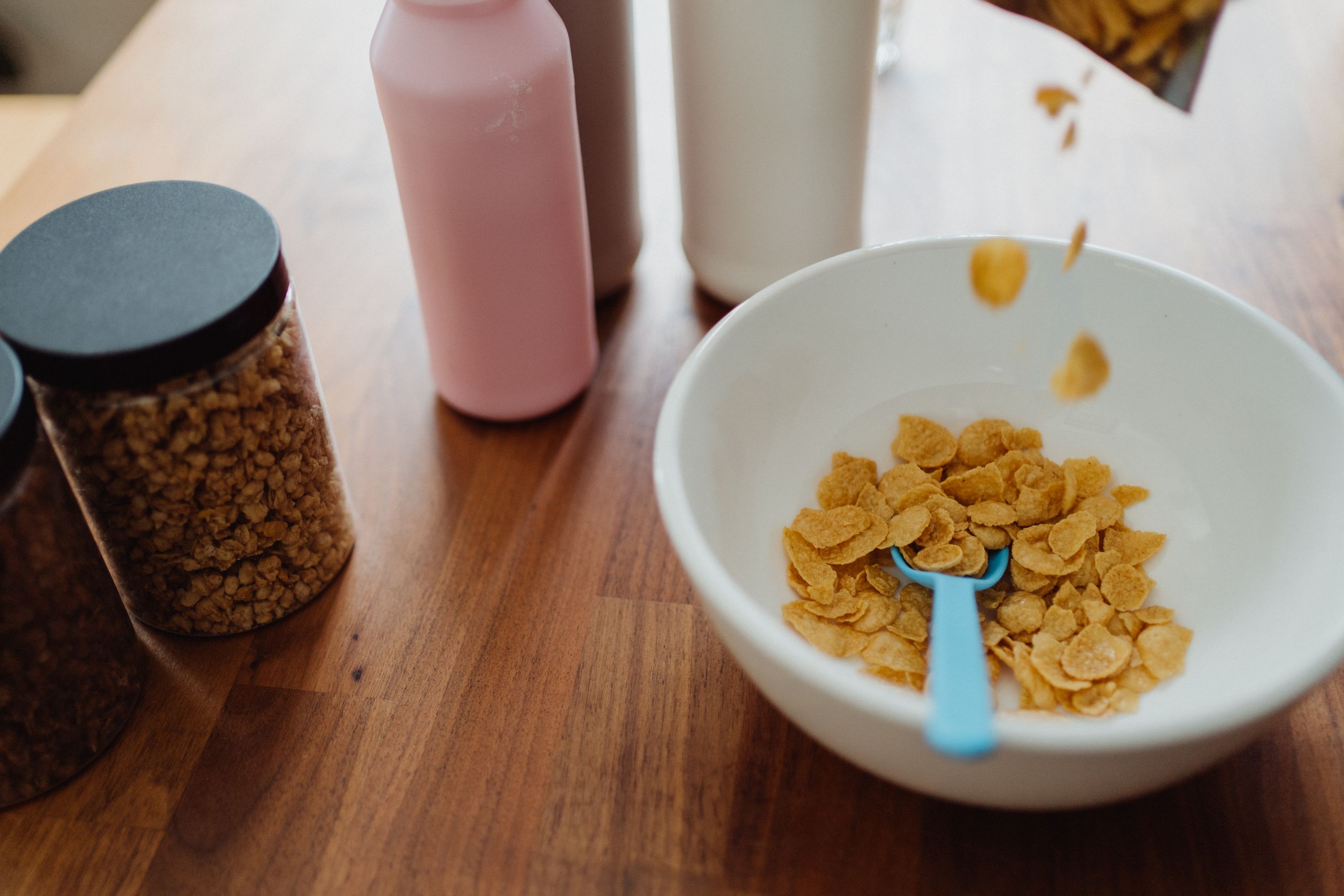 A cozy setup of cornflakes, milk, and granola jars on a wooden table.
