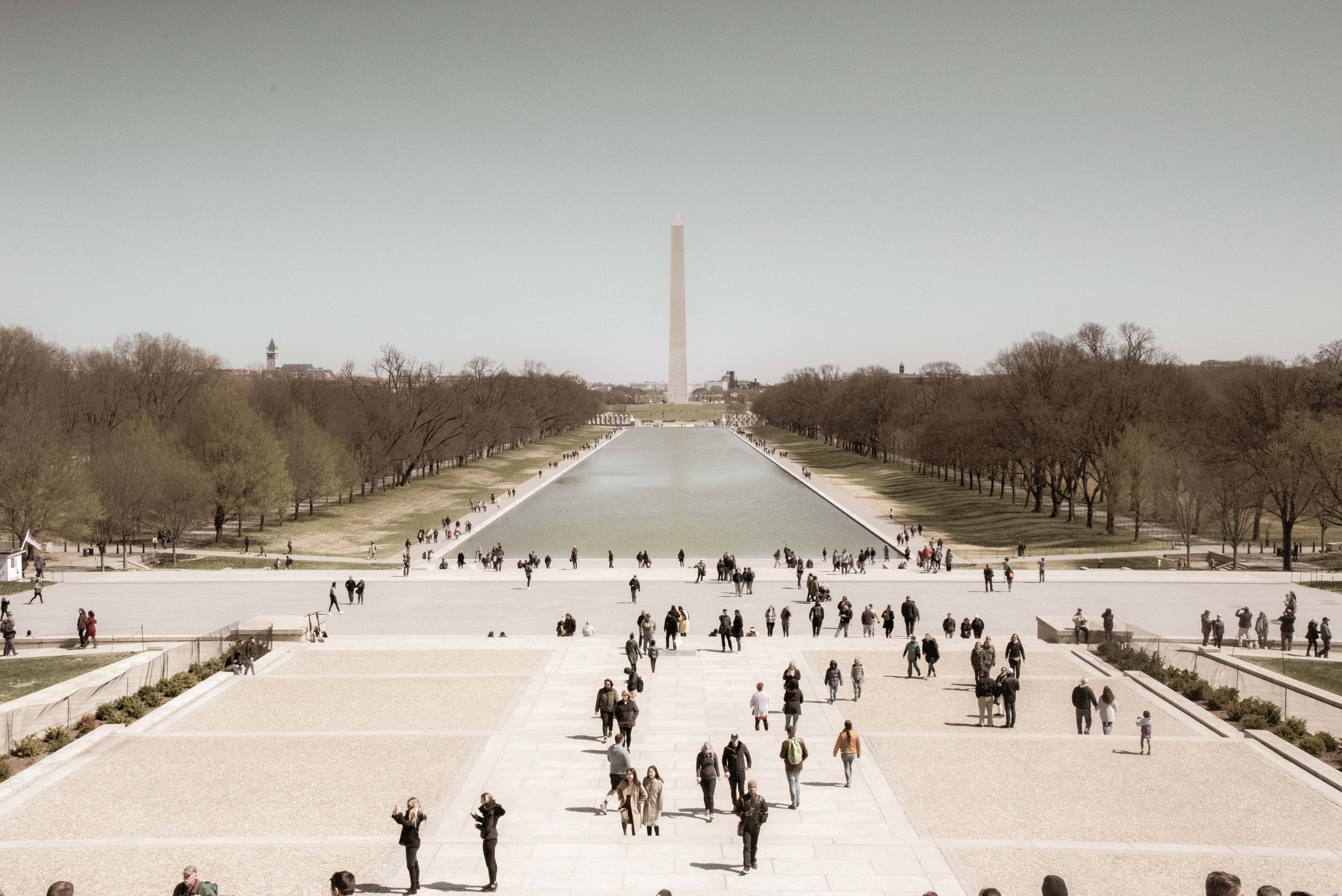 A crowd enjoys a sunny day at the Washington Monument Reflection Pool, a popular tourist spot in Washington, D.C.