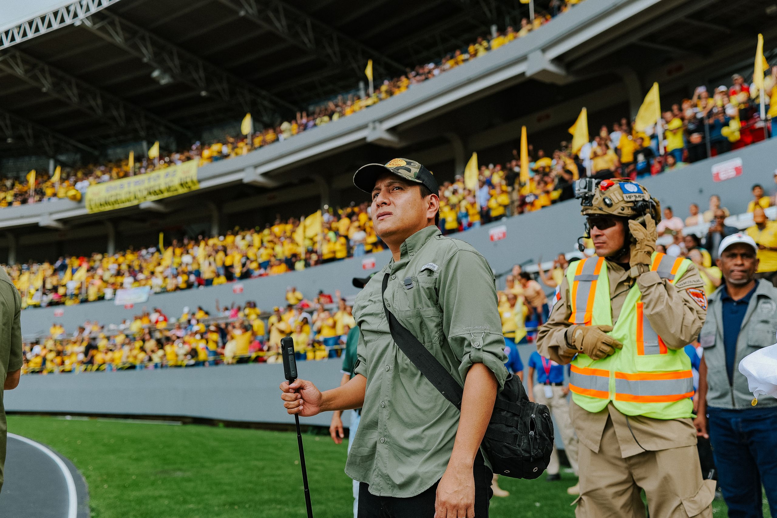 A crowded stadium scene with people in vibrant outfits, highlighting security presence and excitement.