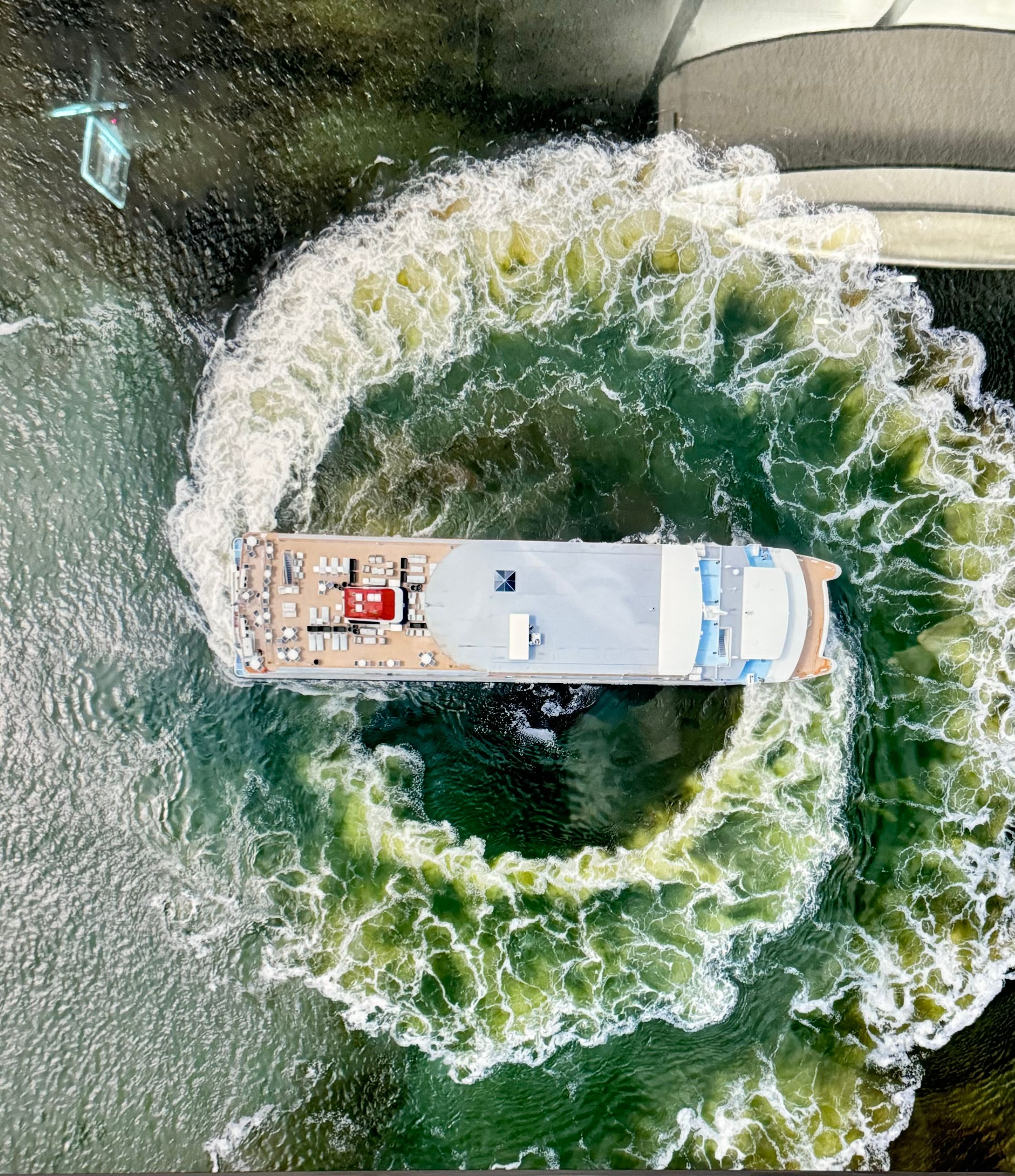 A cruise ship makes a dramatic circular wake in the ocean, seen from above.