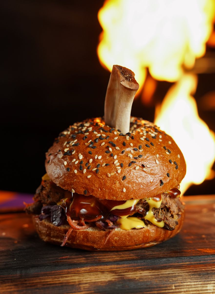 A delicious gourmet hamburger topped with a beef bone, set against a fiery background.