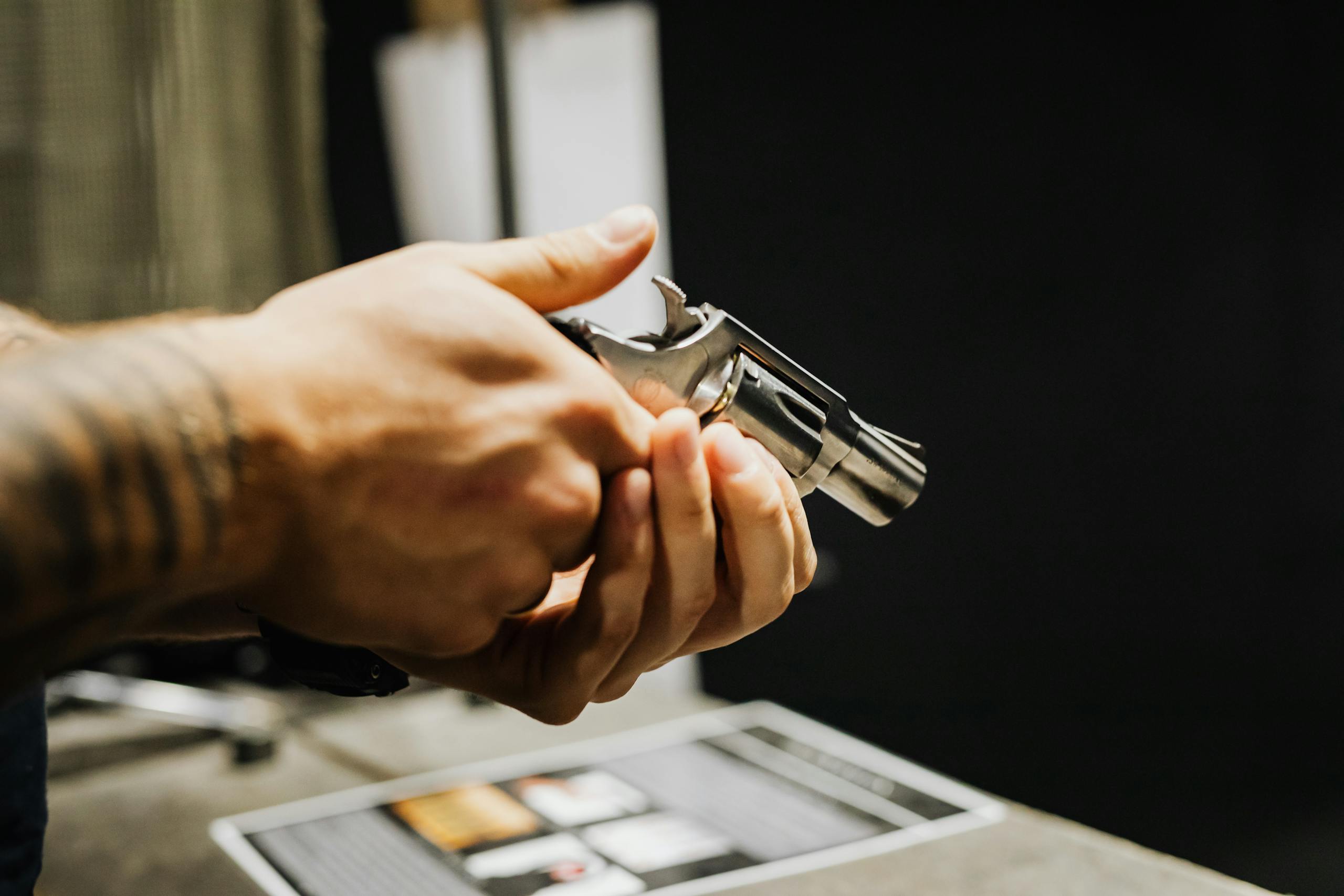 A detailed close-up of a person holding a revolver in an indoor setting. Strong focus on hands and firearm.