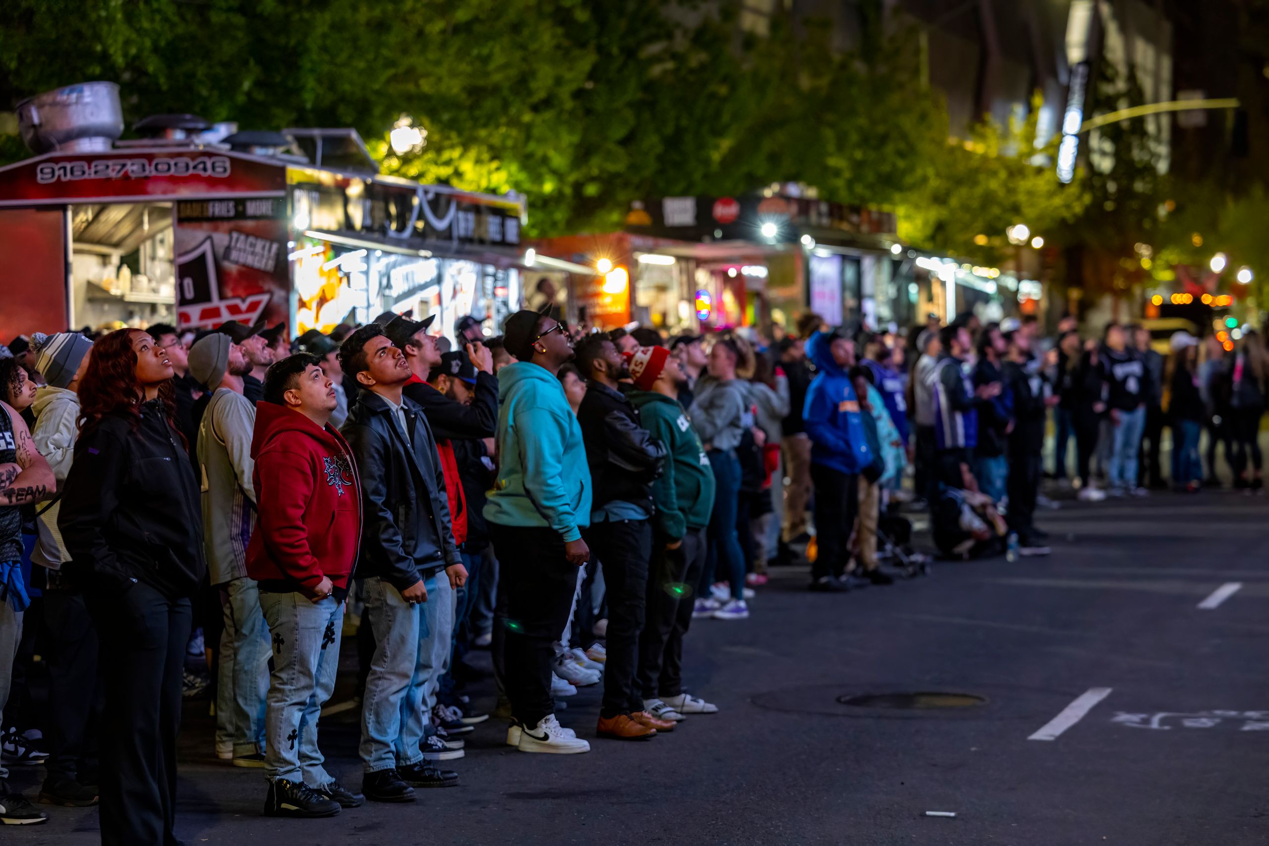 A diverse crowd gathers at a lively street festival with food trucks at night.