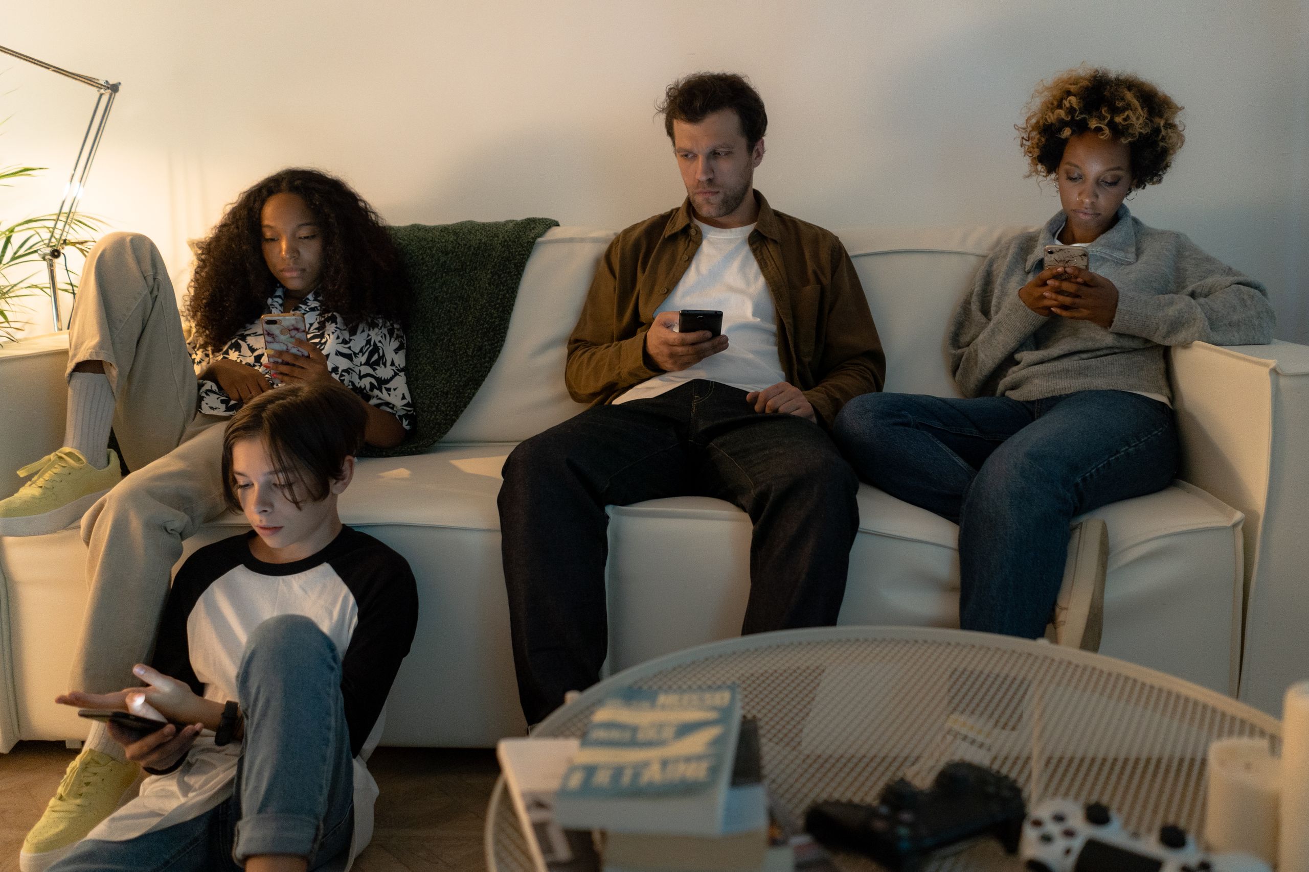 A diverse family sits on a sofa using their smartphones together indoors.