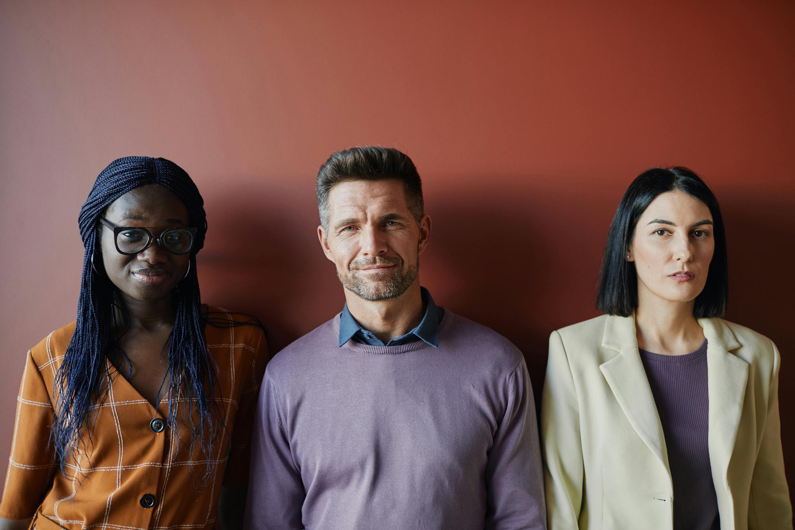 A diverse group of professionals standing against a red background, showcasing teamwork and inclusion.