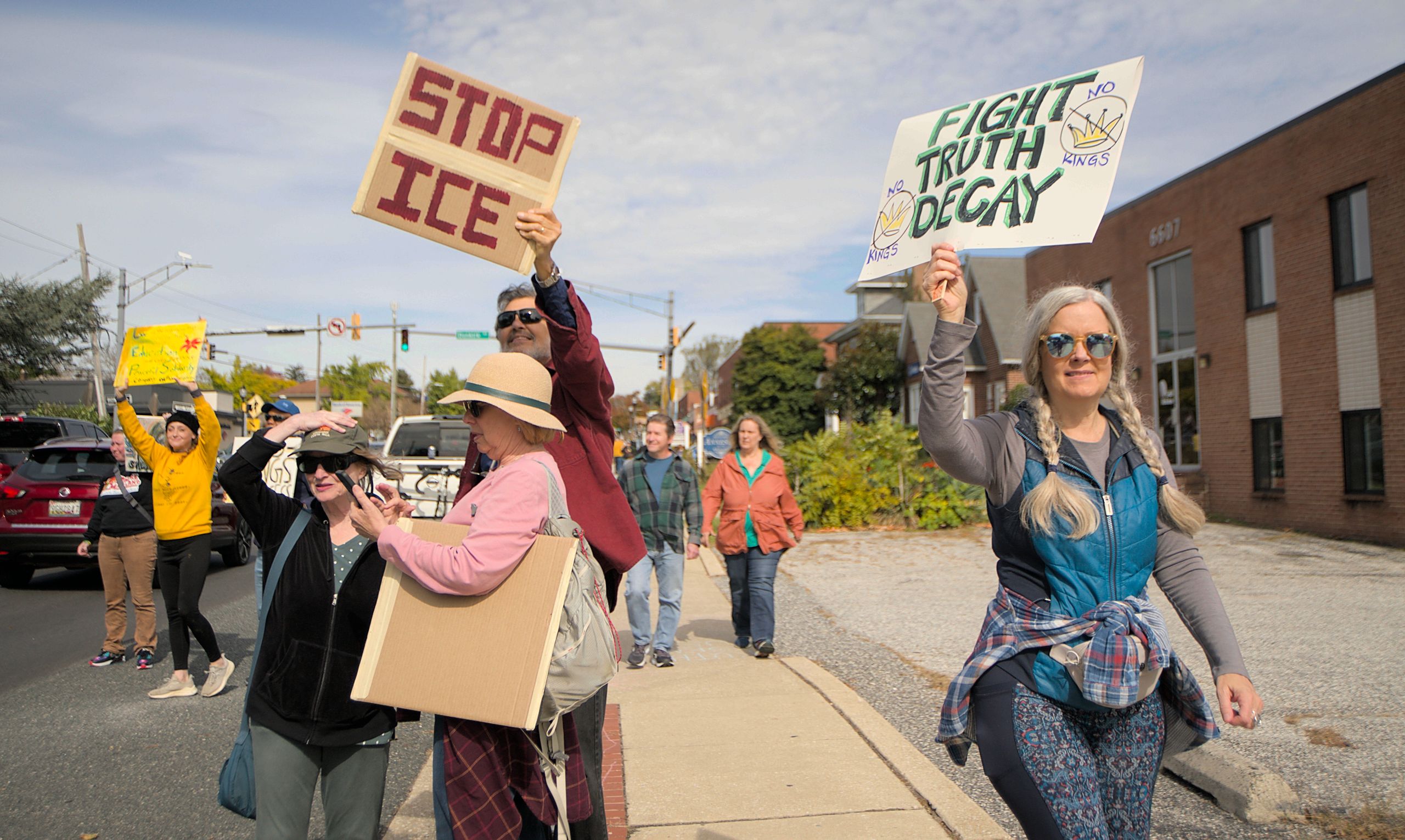 A diverse group peacefully protests in Towson, Maryland, holding signs for various causes.