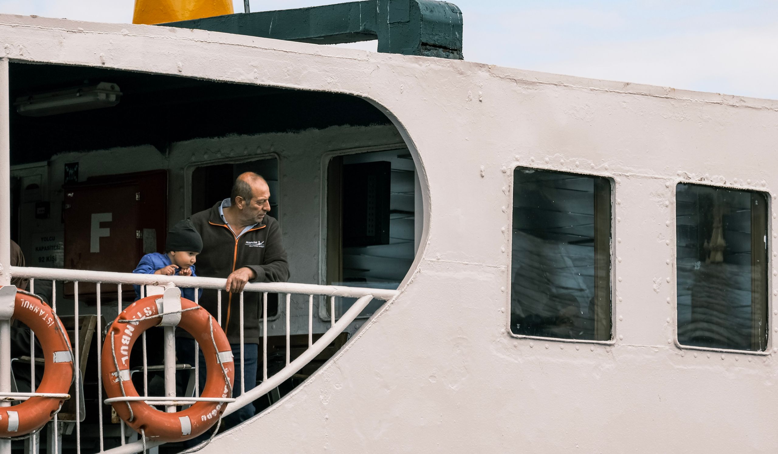 A father and child enjoy a peaceful moment on a boat deck, looking at the view.
