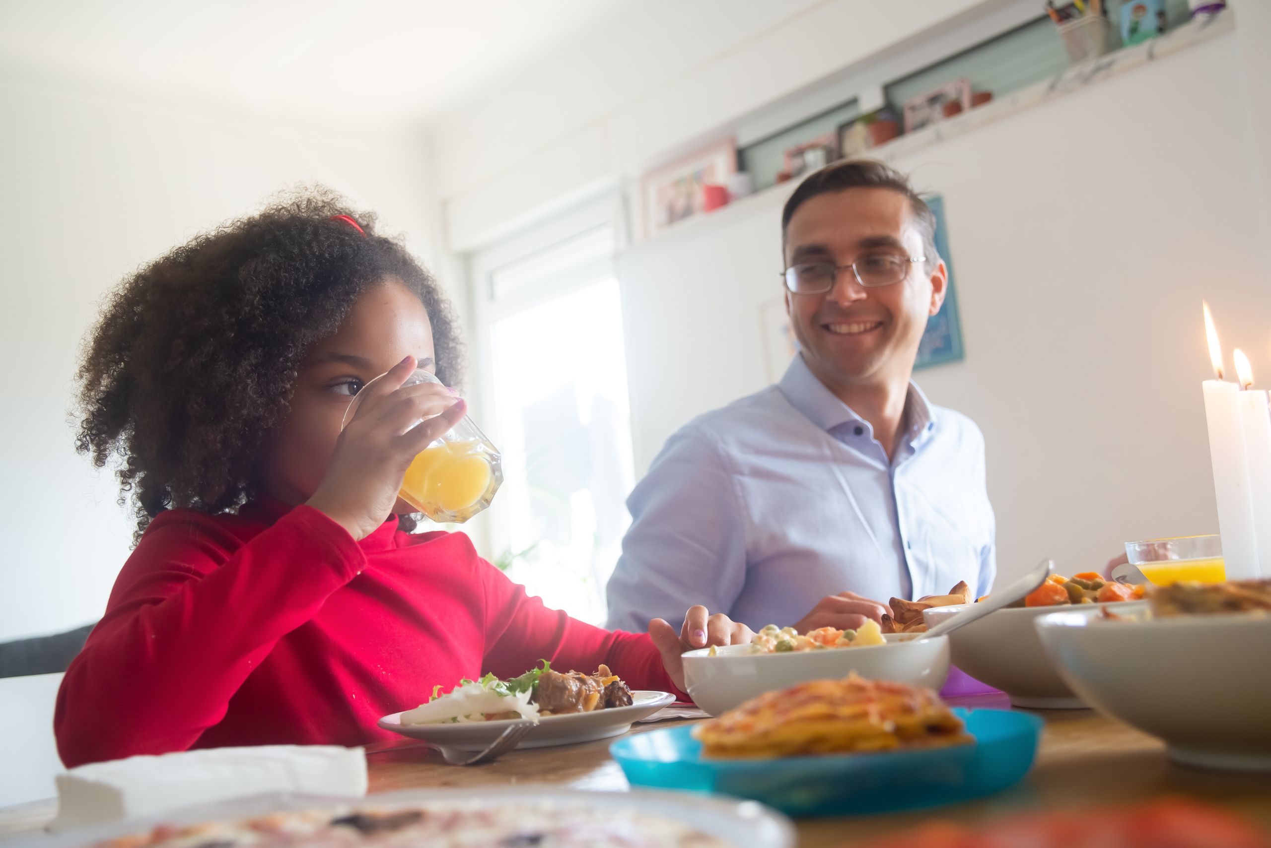 A father and daughter share a joyful lunch indoors, highlighting family bonding and mealtime.