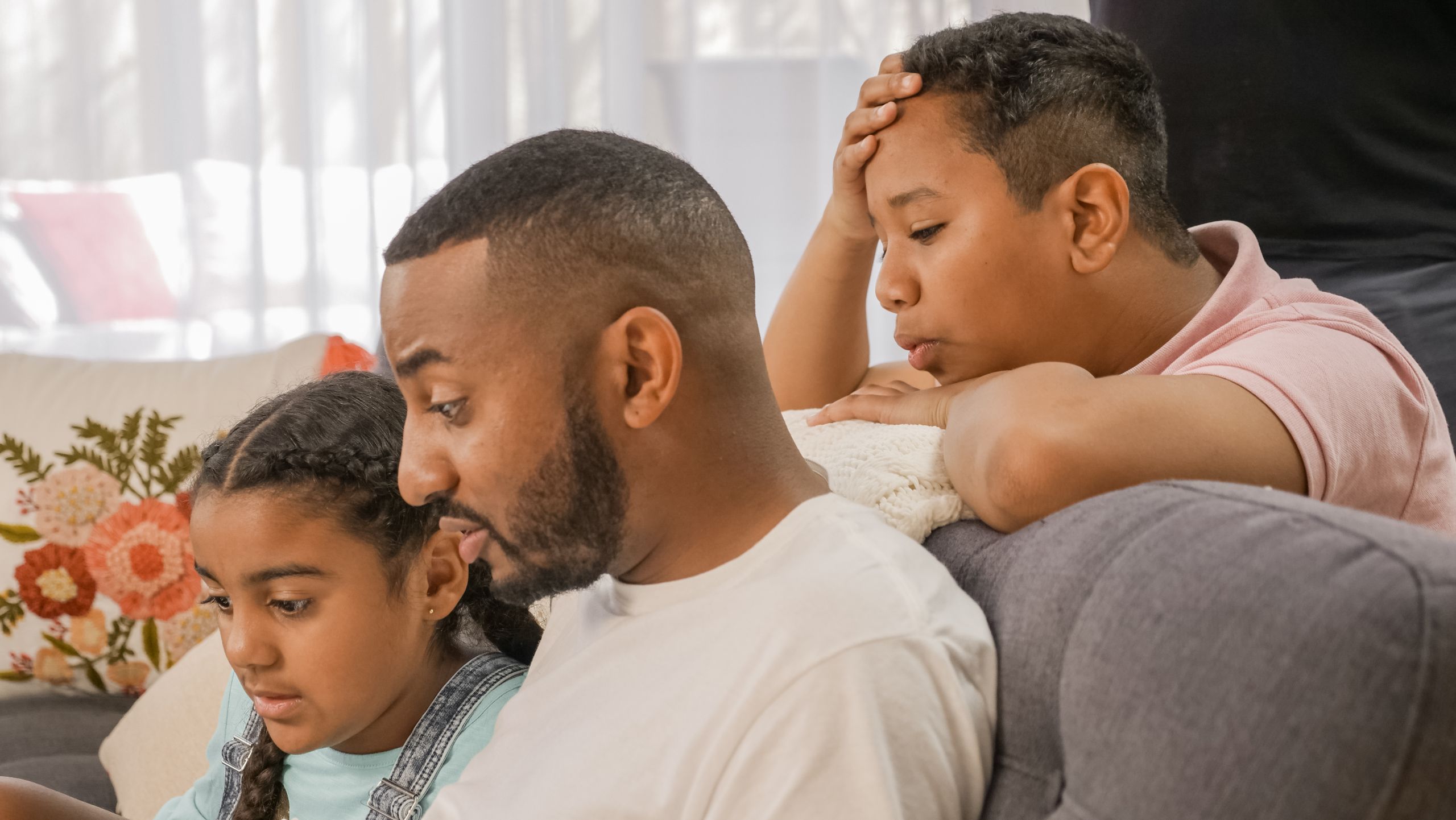 A father and his children engaged in an educational activity at home using a laptop.