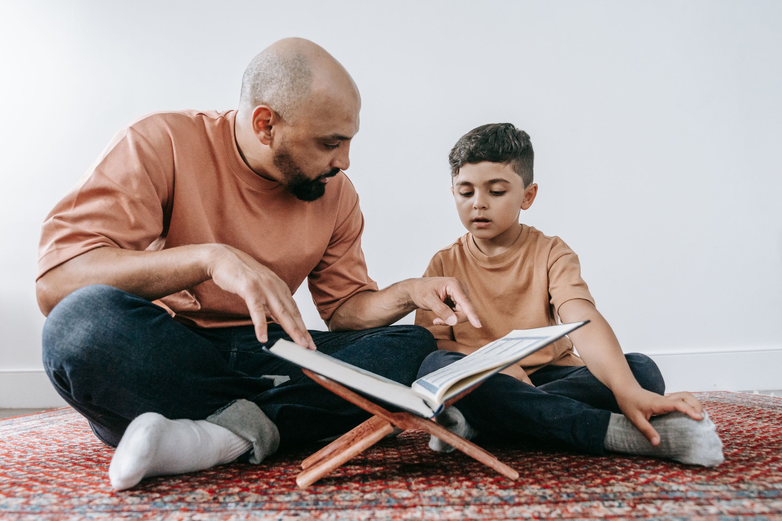 A father guides his son in reading a book, promoting learning and bonding.