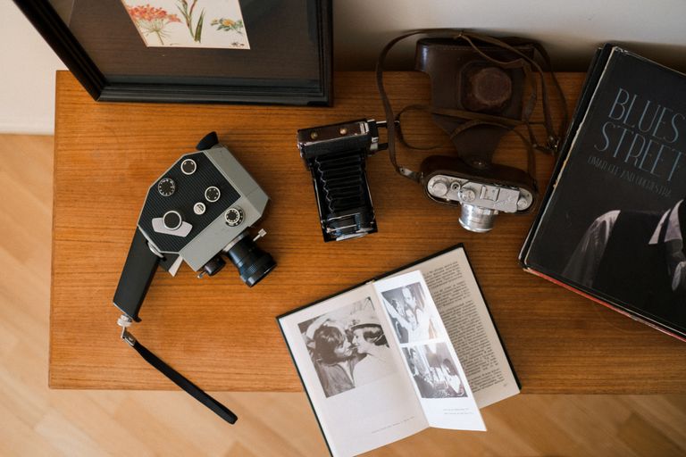 A flat lay of vintage cameras, a book, and photos on a wooden desk.