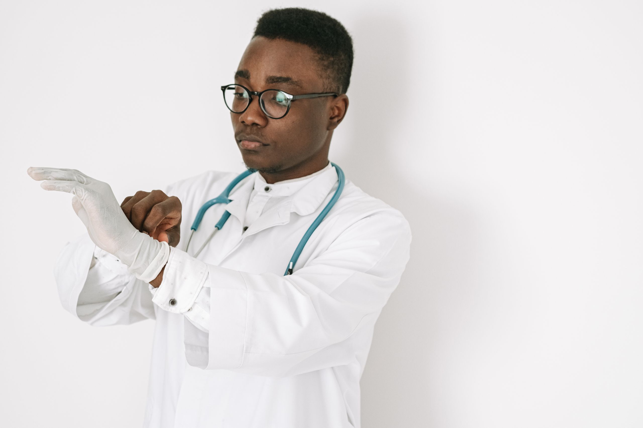 A focused doctor in a medical gown and eyeglasses putting on gloves, symbolizing professionalism.