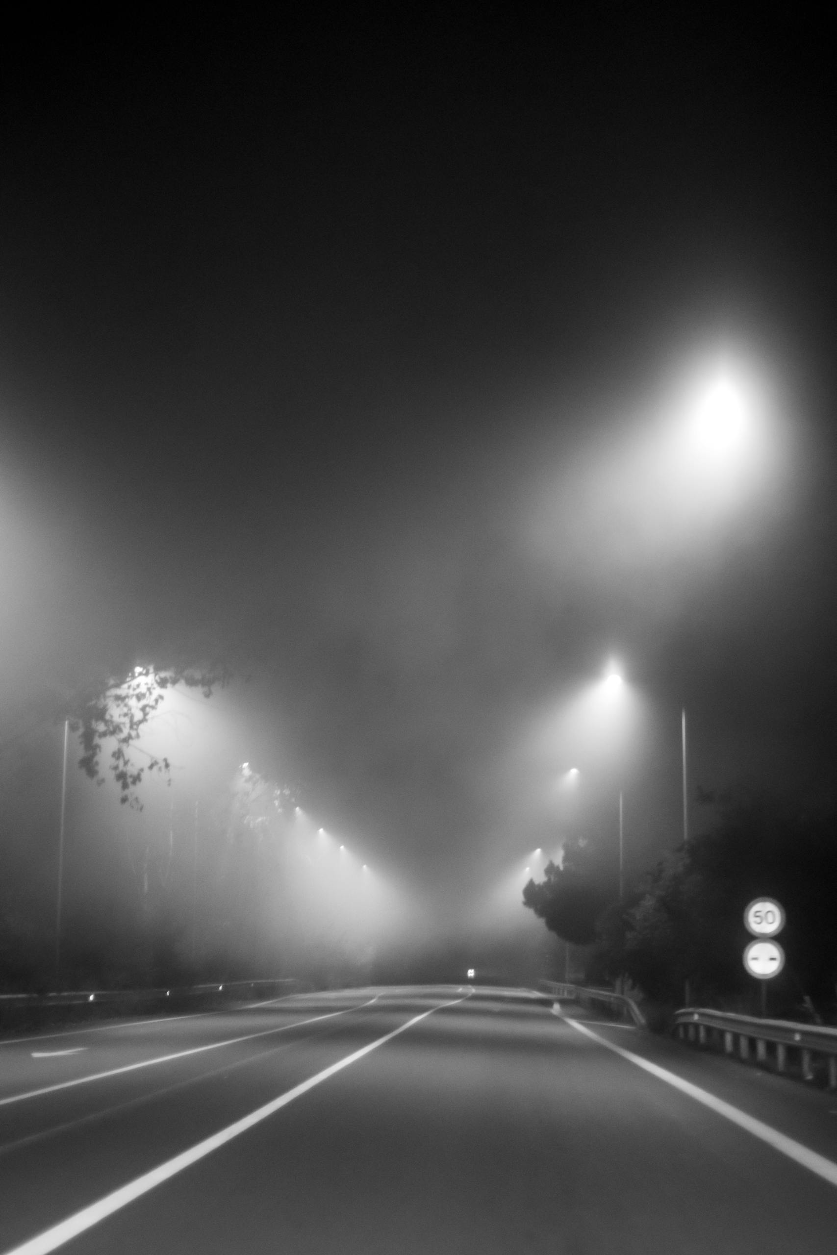 A foggy night scene with streetlights illuminating an empty road, creating a mysterious atmosphere.
