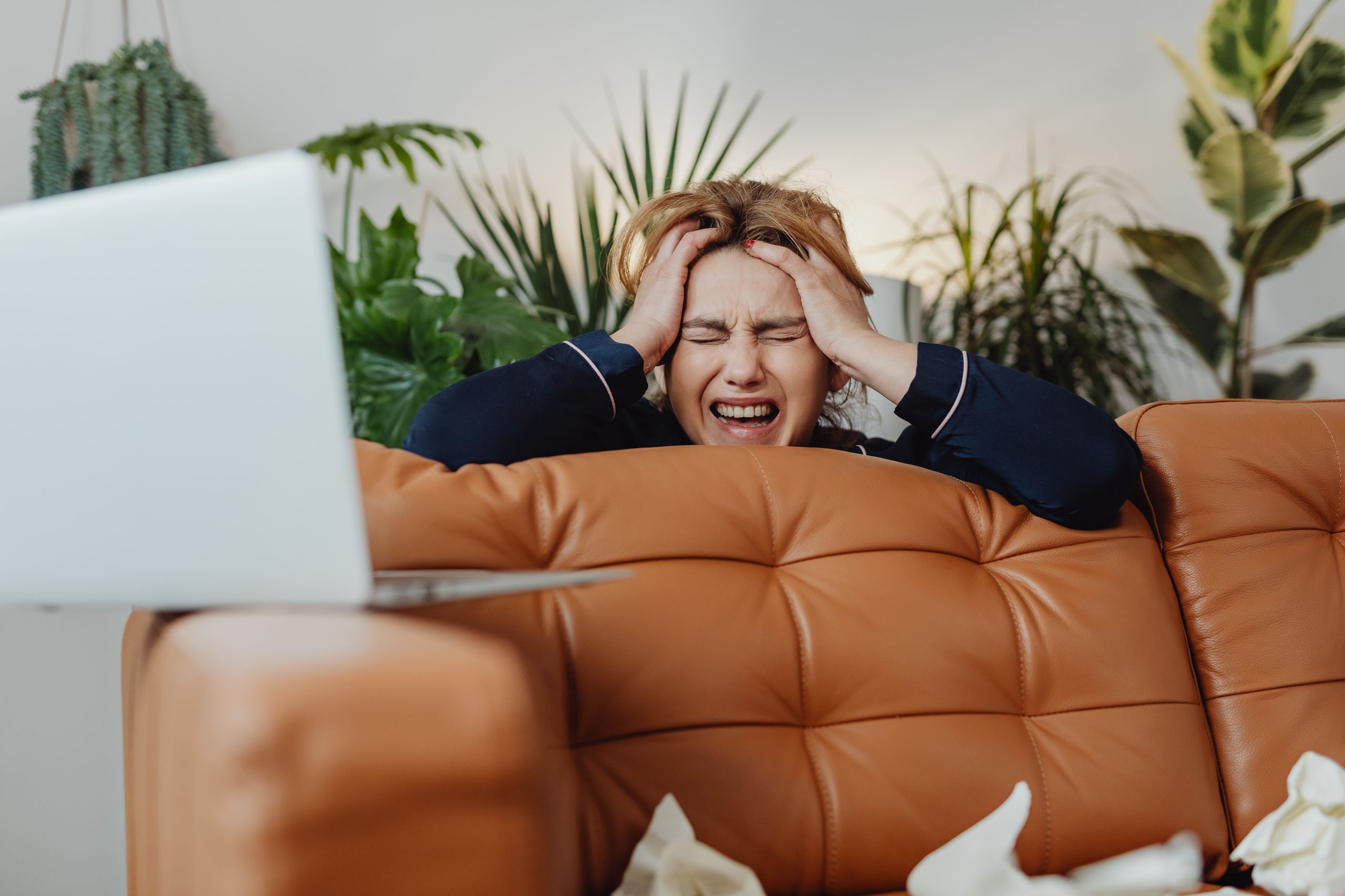 A frustrated woman with eyes closed, sitting on a sofa, experiencing stress at home.
