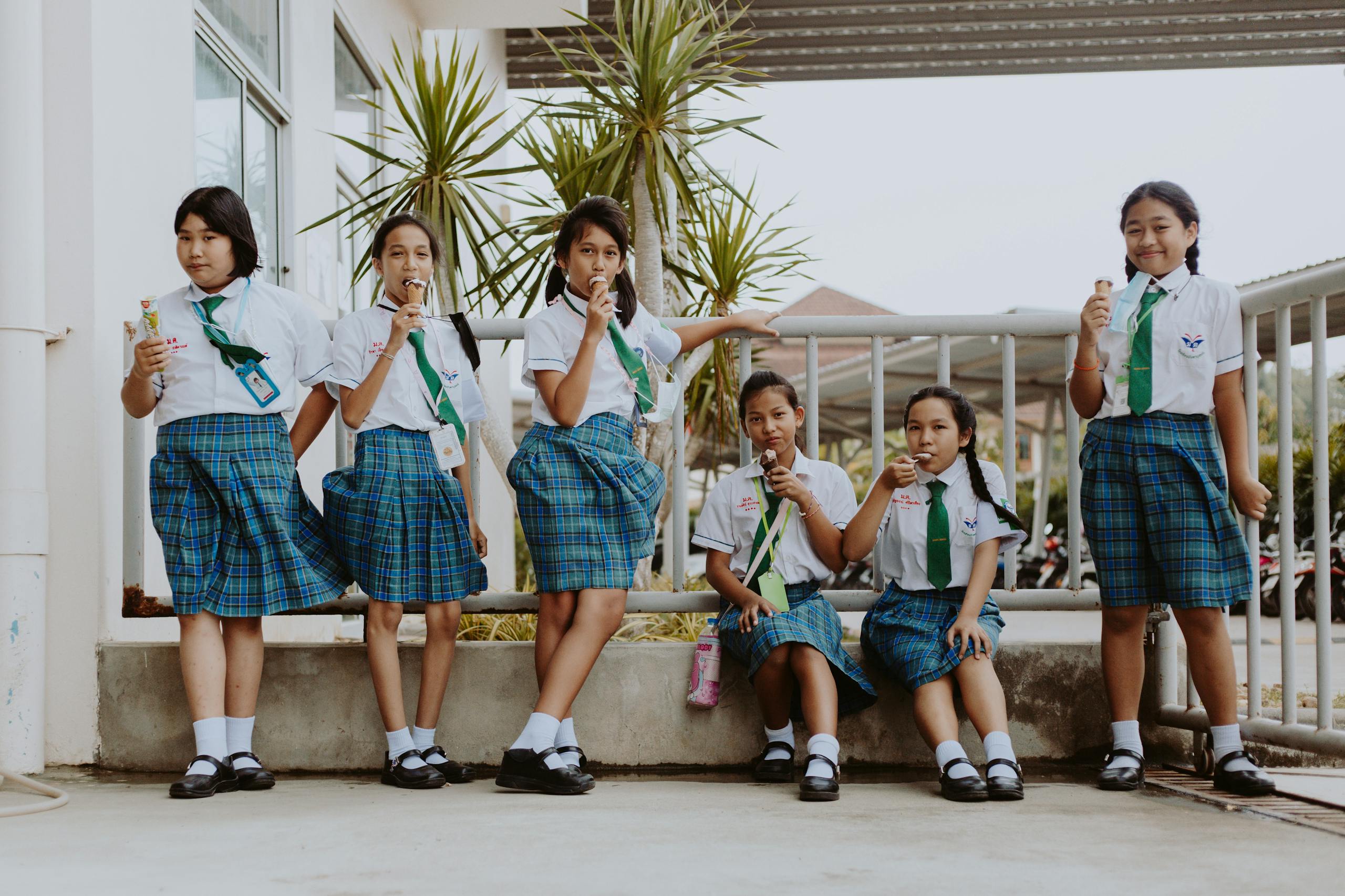 A group of schoolgirls in uniform enjoying ice cream together during a break outdoors.