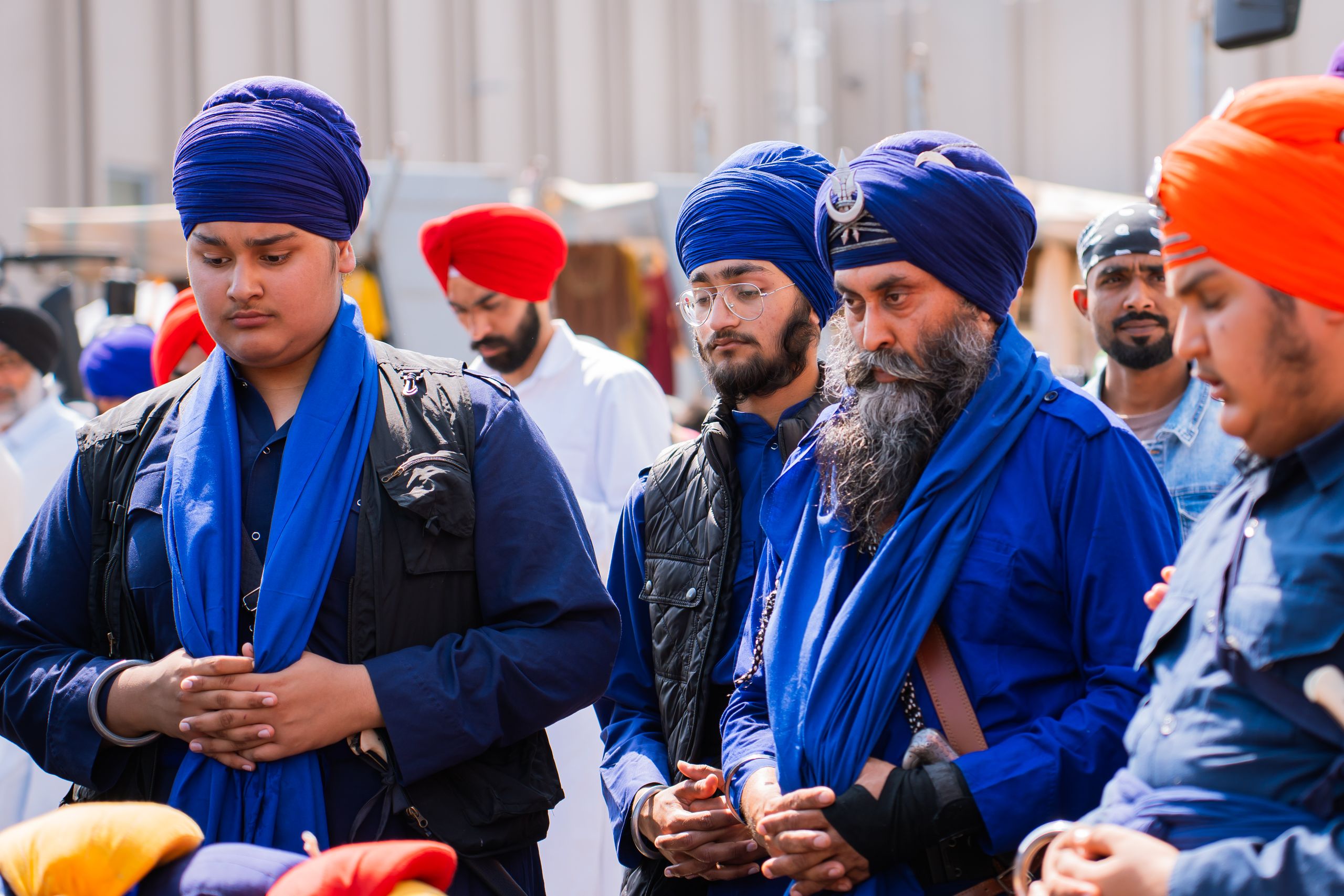 A group of Sikh men wearing traditional blue turbans participate in a peaceful assembly outdoors.