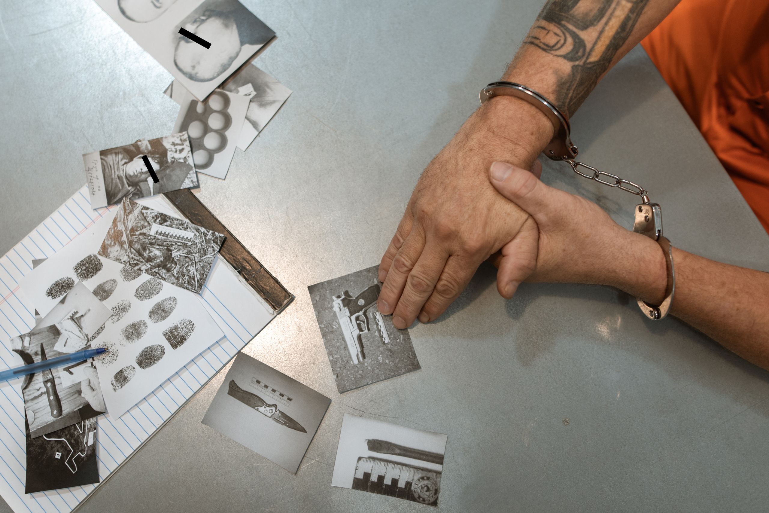 A handcuffed individual examines evidence photos and documents during an investigation.