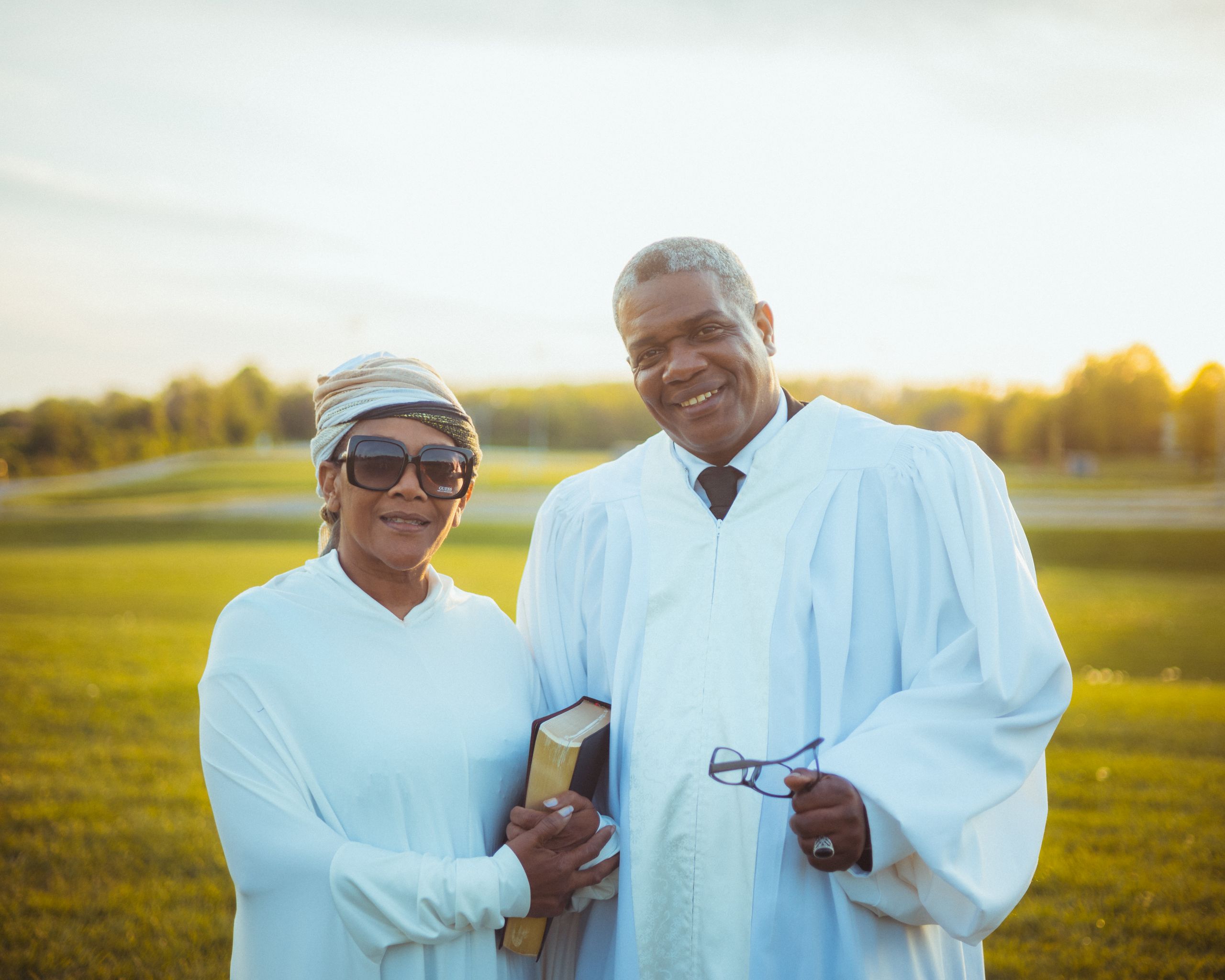A happy couple of ministers in white robes enjoying a sunny outdoor setting, embodying spirituality and joy.