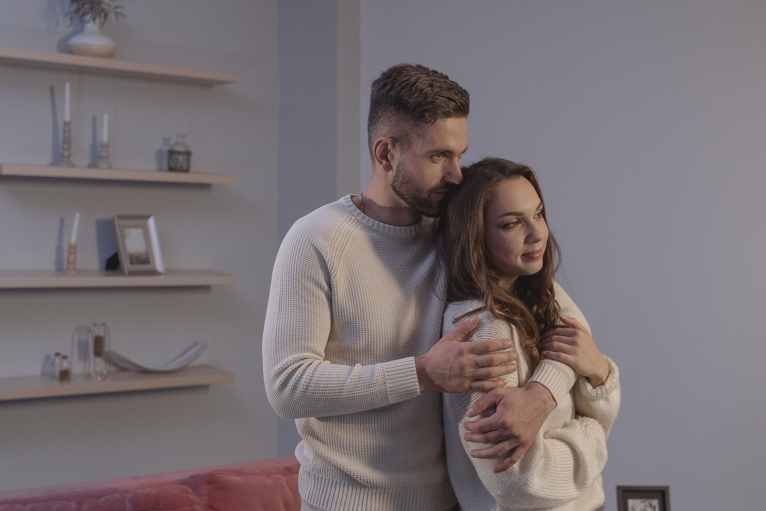 A loving couple embraces warmly in a modern indoor setting, expressing affection and togetherness.