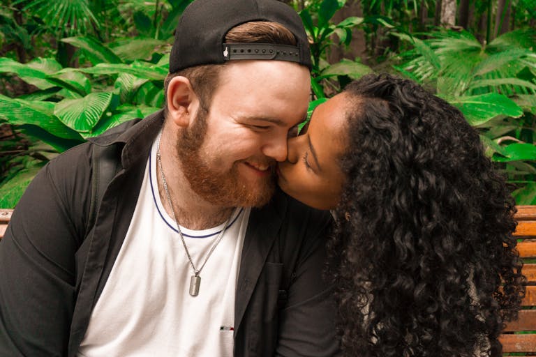 A loving couple kisses tenderly while seated outdoors in lush greenery, showcasing affection and intimacy.