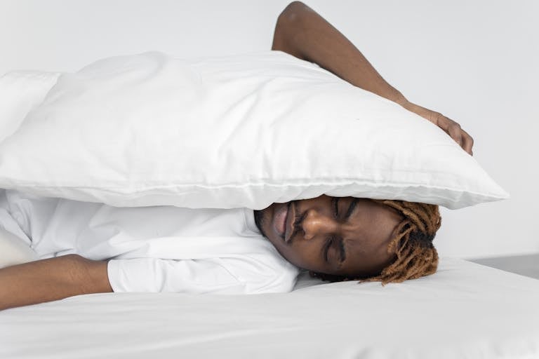 A man enjoying a peaceful nap indoors under a white pillow, conveying relaxation.